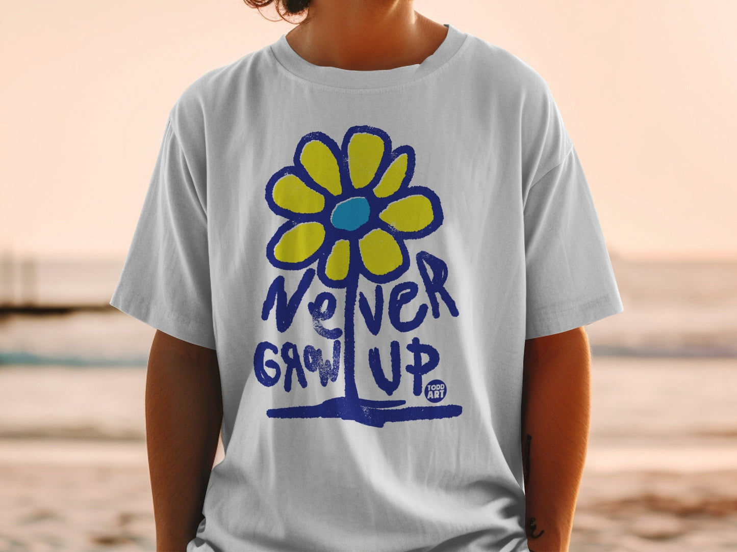 White t-shirt with blue and yellow flower graphic and "Never Grow Up" text.