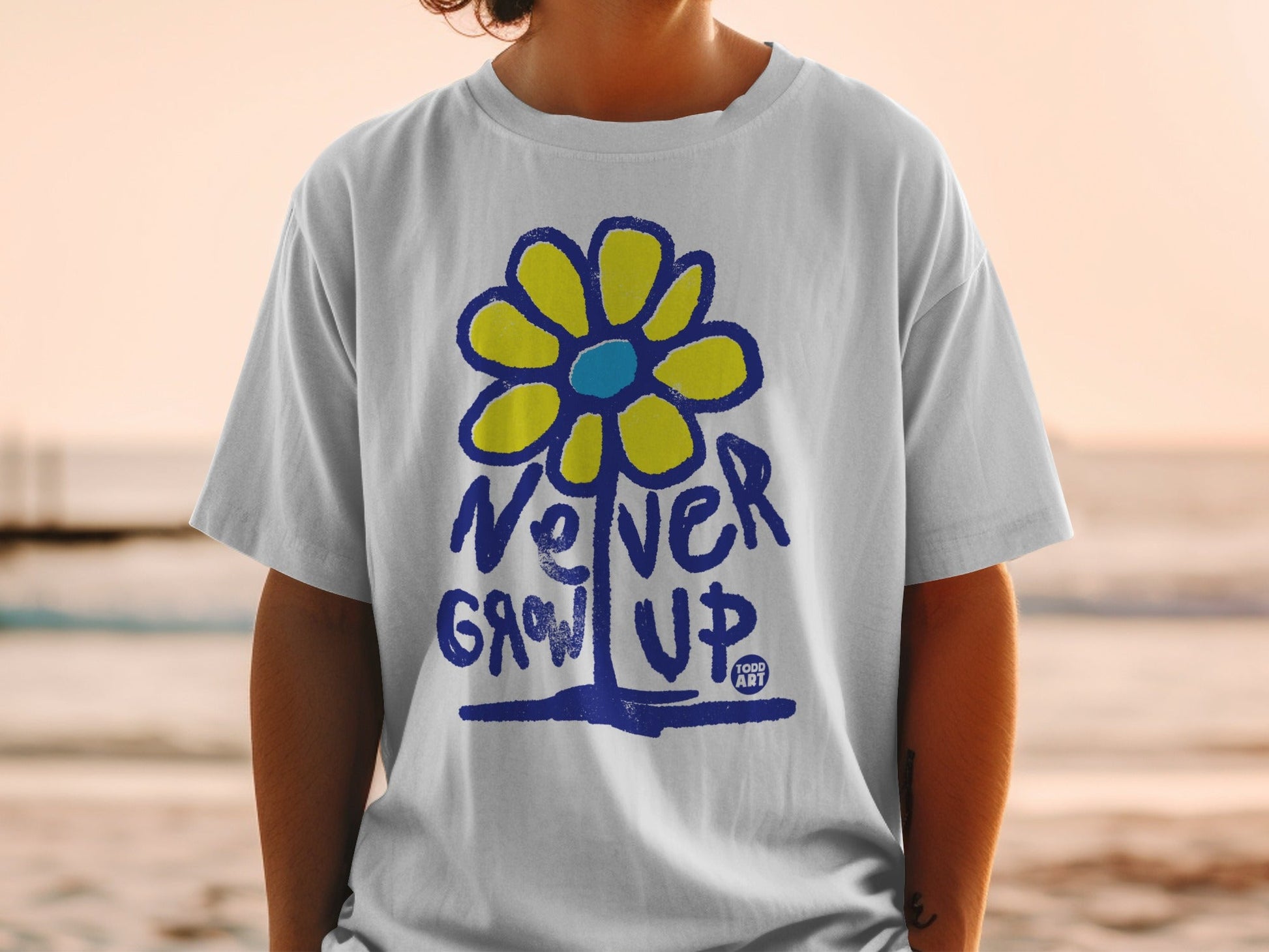 White t-shirt with blue and yellow flower graphic and "Never Grow Up" text.