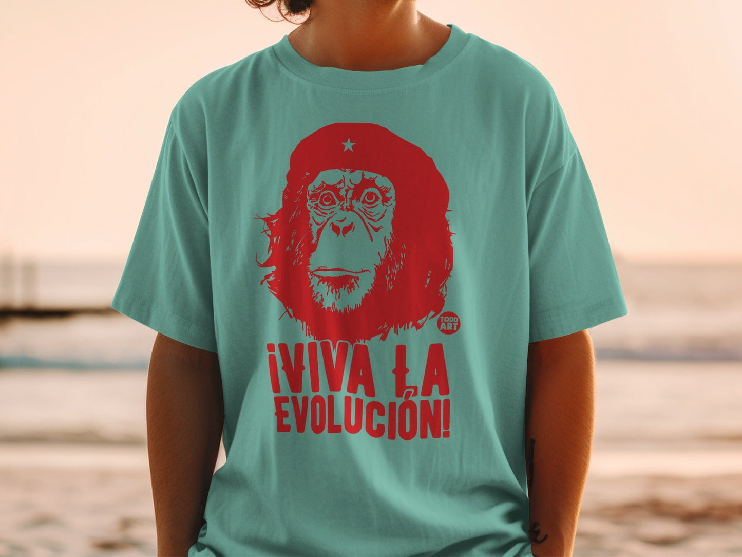 Red primate graphic with ¬°VIVA LA EVOLUCI√ìN! text on teal t-shirt.