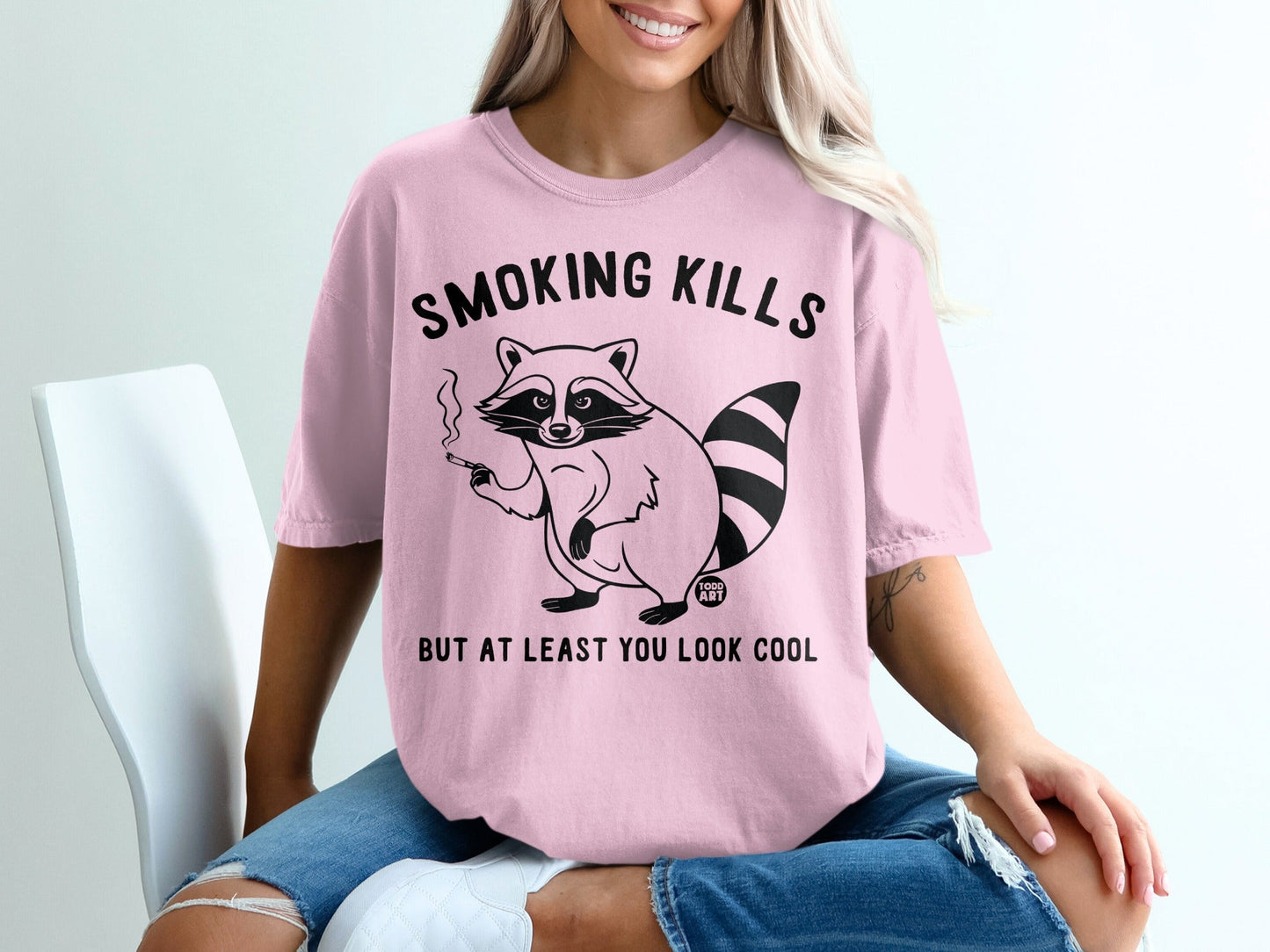 Pink t-shirt with smoking raccoon graphic and text "SMOKING KILLS BUT AT LEAST YOU LOOK COOL".