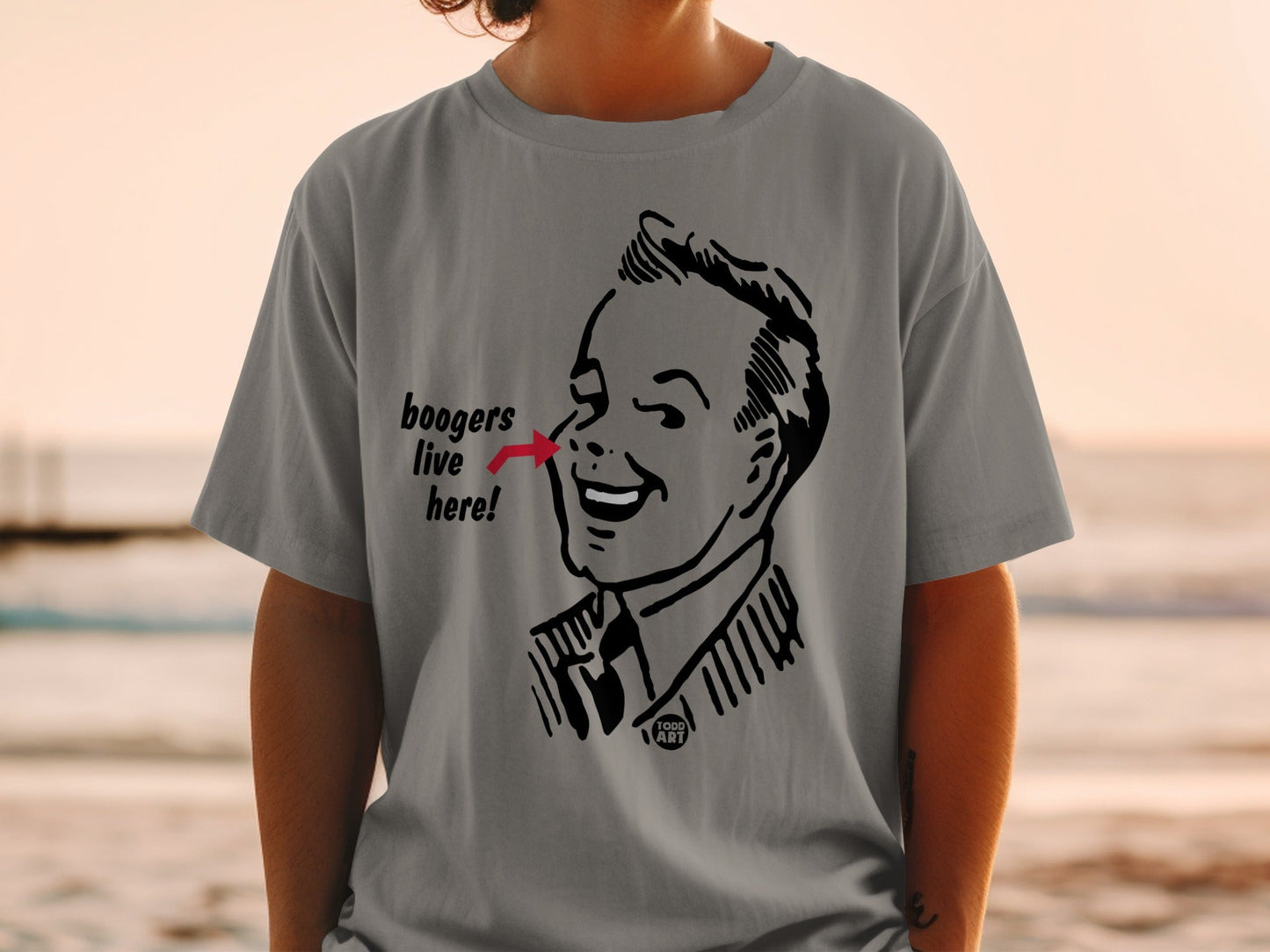 Grey t-shirt with black line art of a man pointing to his nose with "boogers live here!" text.