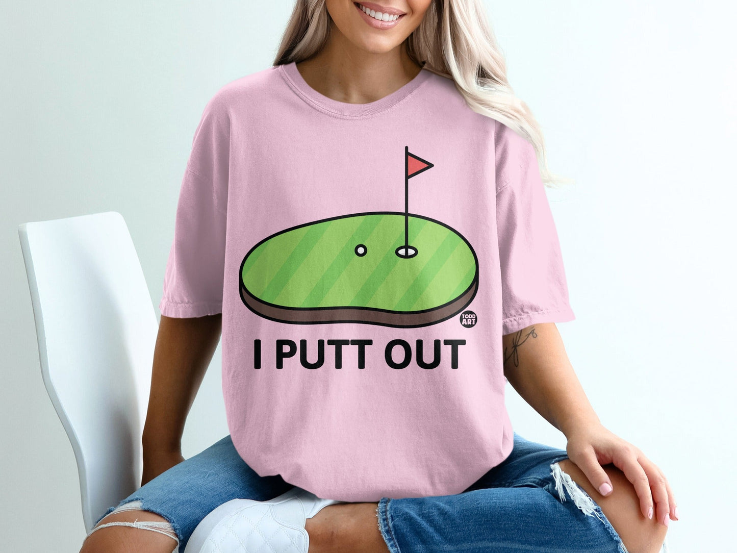 Pink t-shirt with a cartoon golf green and "I PUTT OUT" text.