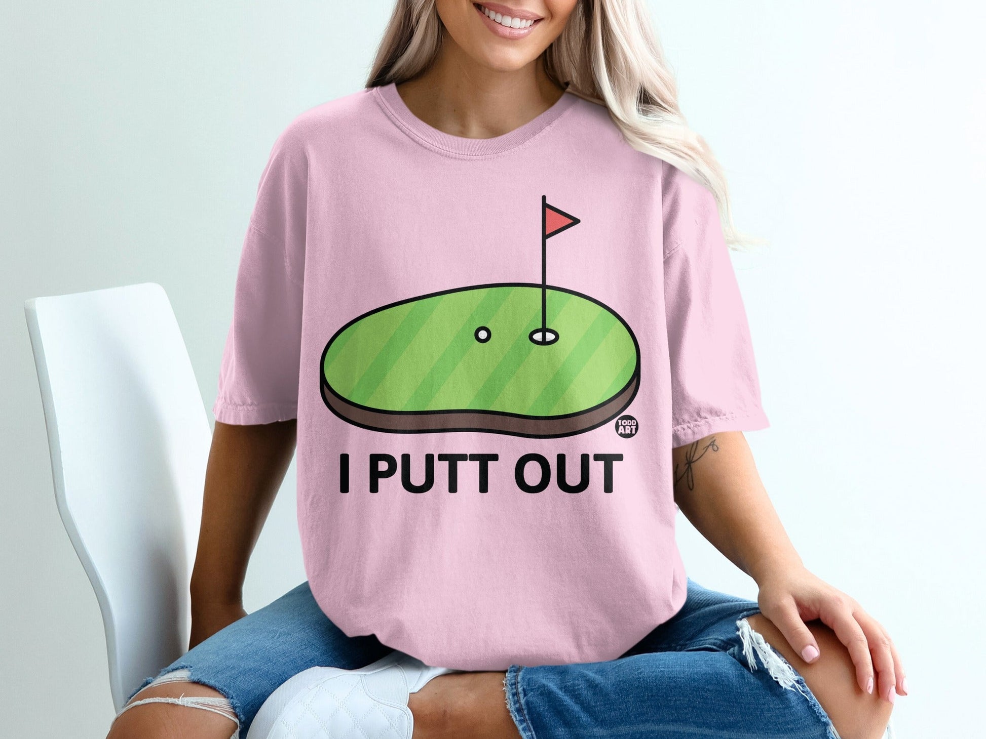 Pink t-shirt with a cartoon golf green and "I PUTT OUT" text.