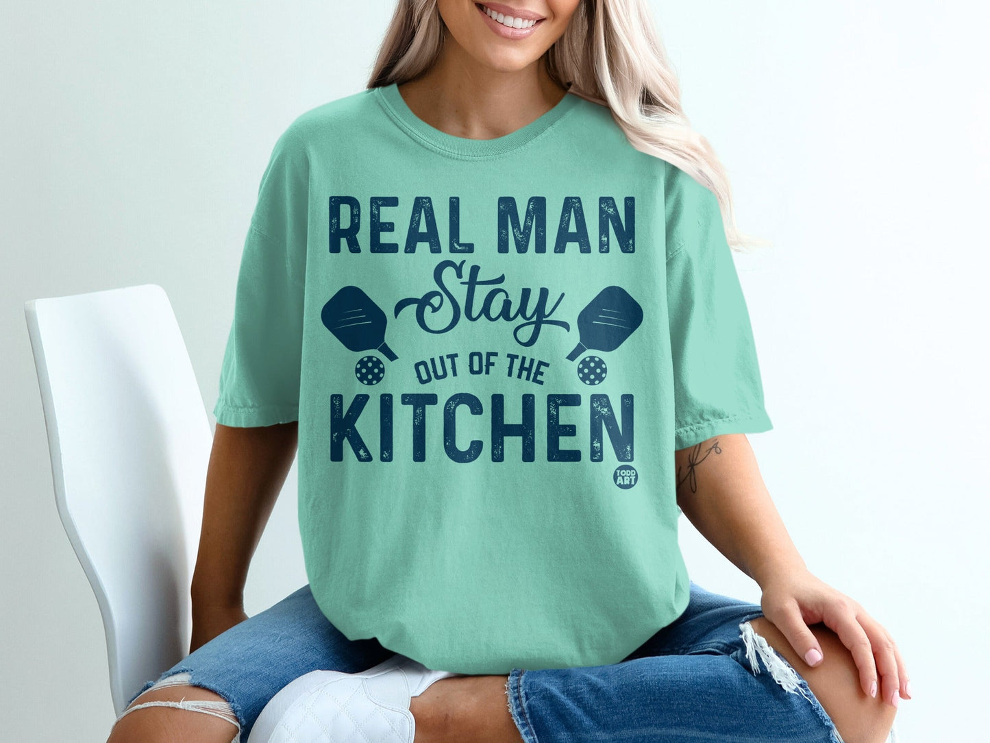 Teal t-shirt with "Real Man Stay Out of the Kitchen" text and pickleball paddles.