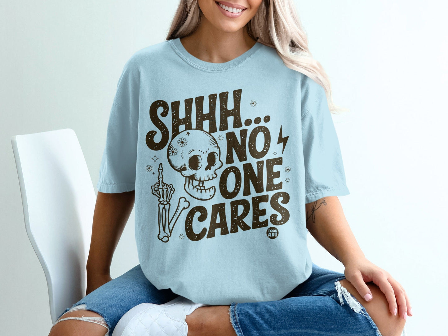 Light blue t-shirt with "SHHH... NO ONE CARES" and skeleton hand flipping the bird.