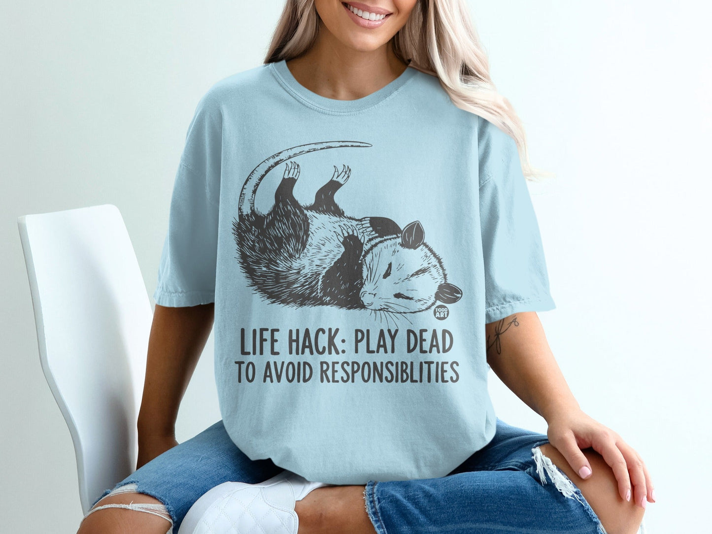 Light blue t-shirt with opossum graphic and text "LIFE HACK: PLAY DEAD TO AVOID RESPONSIBILITIES".