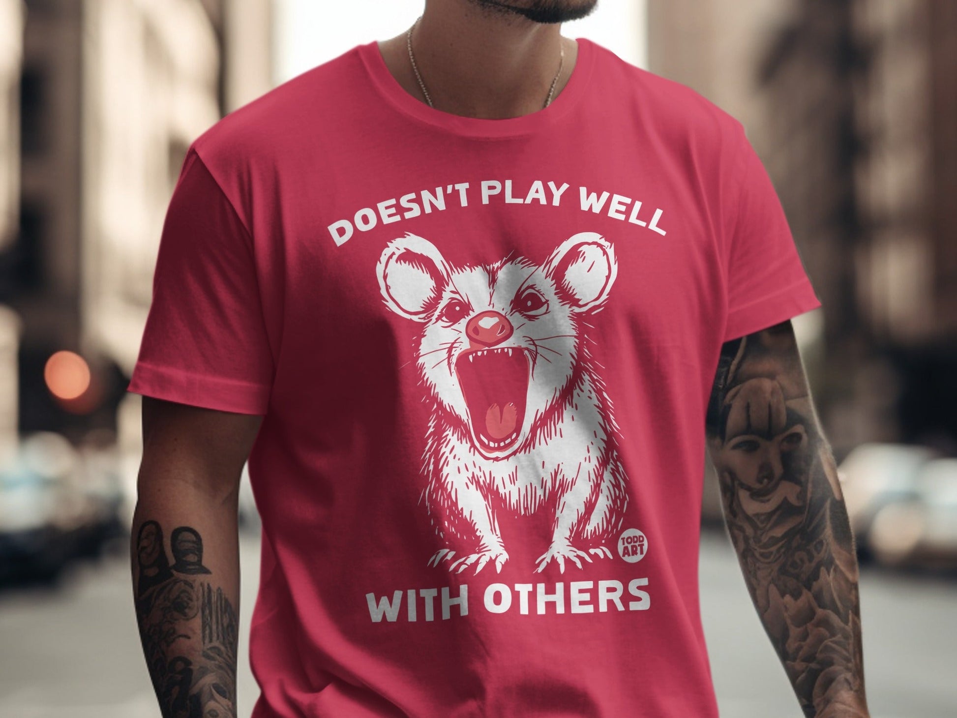 Red t-shirt with white opossum illustration and "Doesn't Play Well With Others" text.