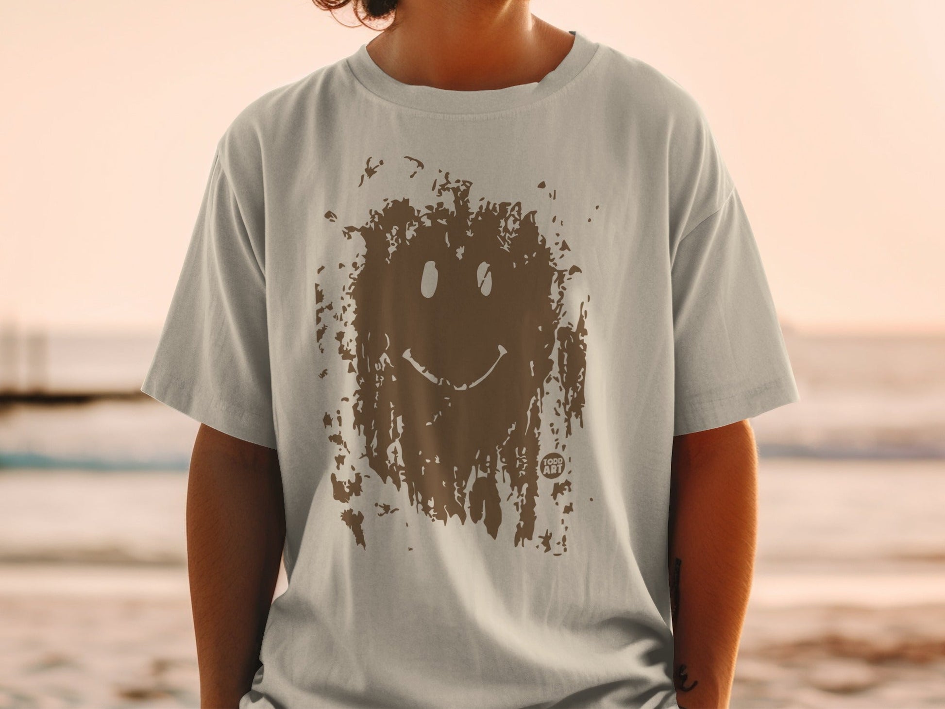 T-shirt with brown distressed smiley face graphic on tan fabric.