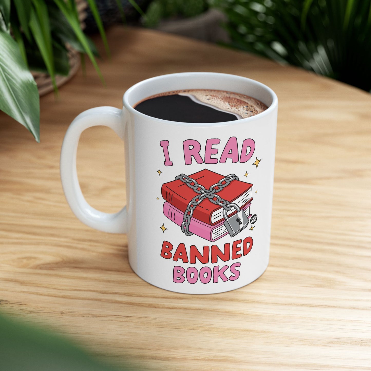 White mug with "I Read Banned Books" text and chained locked books graphic.