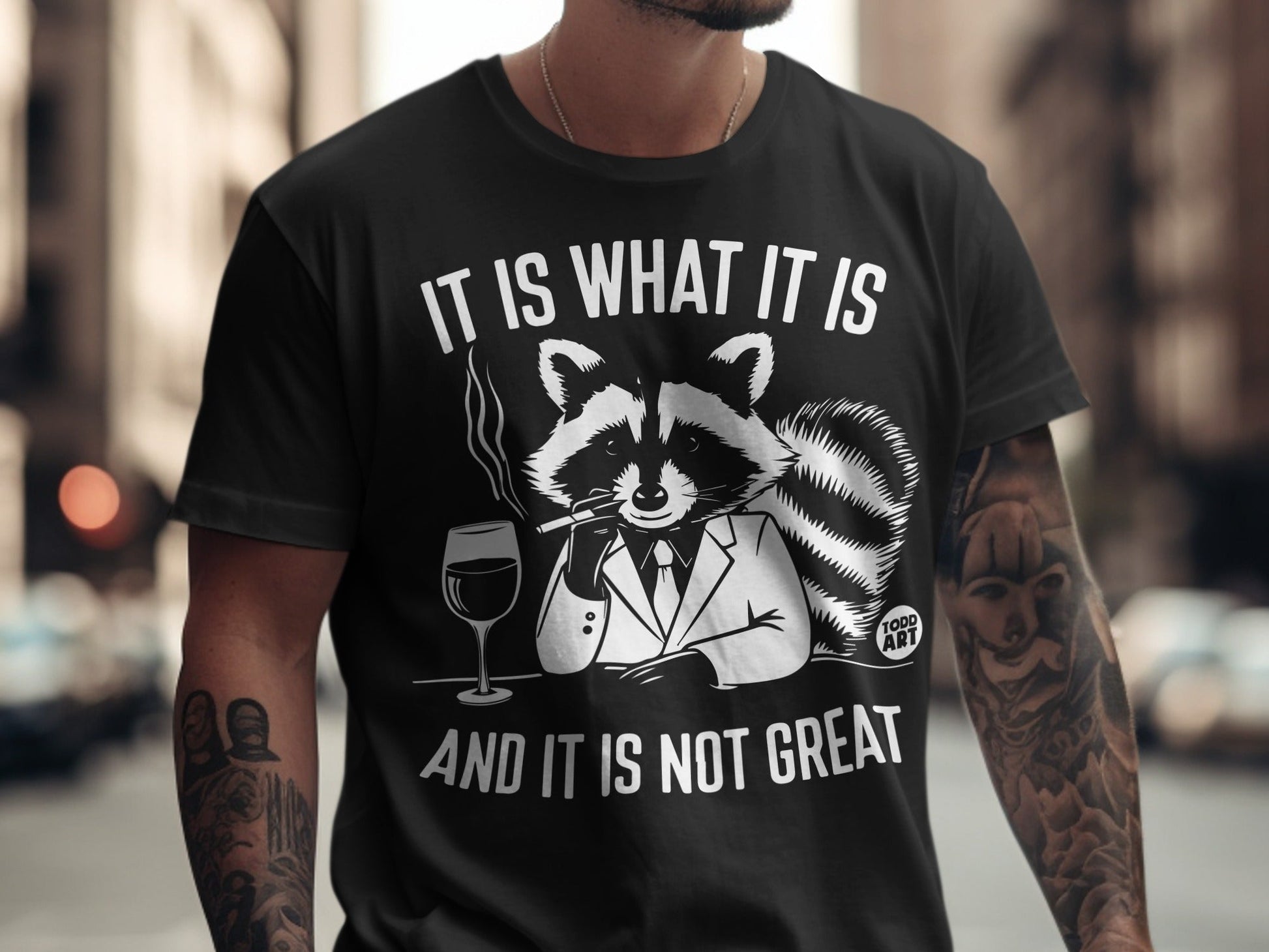 Black t-shirt with raccoon in suit smoking, holding wine, text "It is what it is and it is not great".
