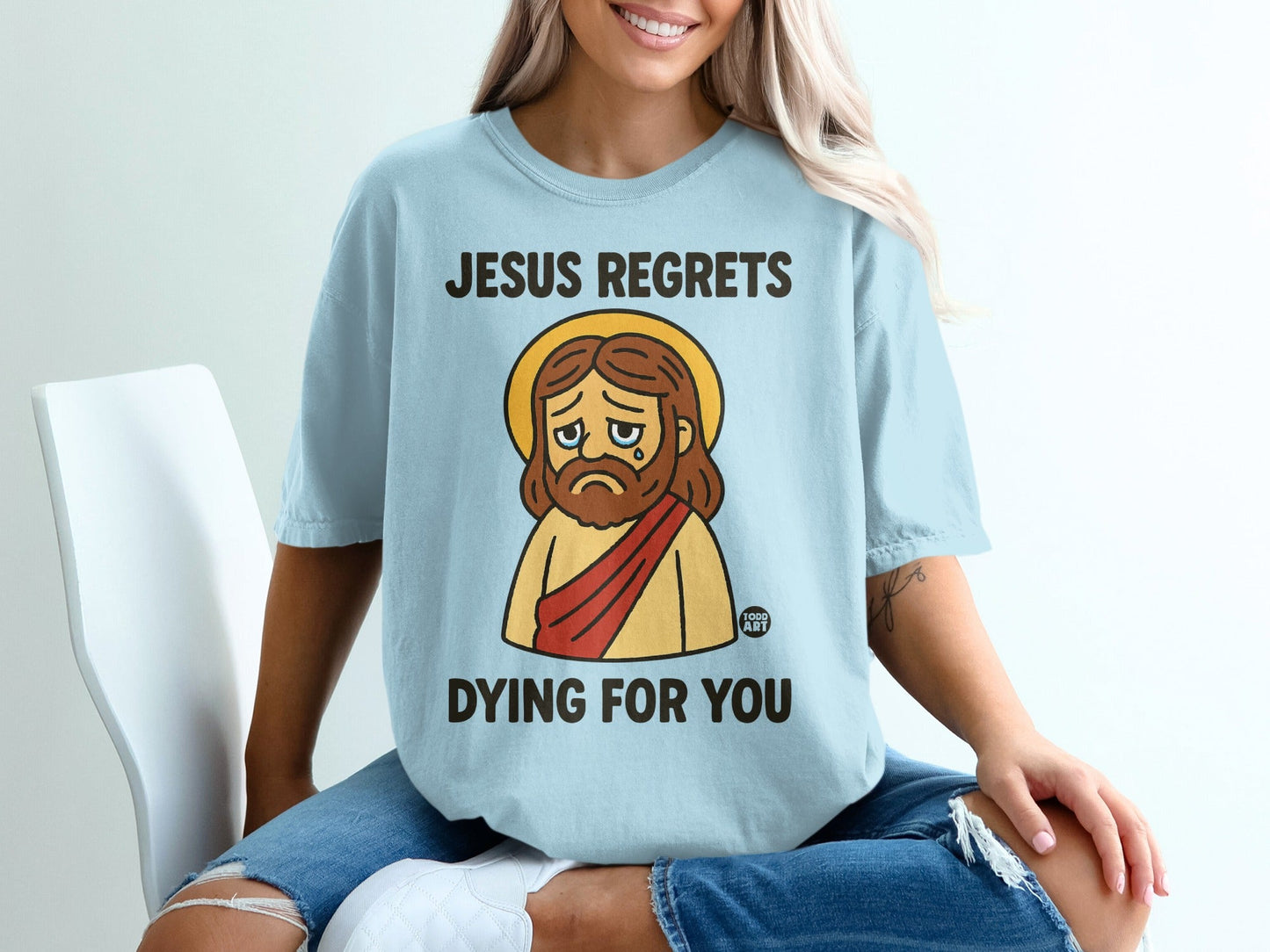 Light blue t-shirt with "Jesus regrets dying for you" text and sad cartoon Jesus graphic.