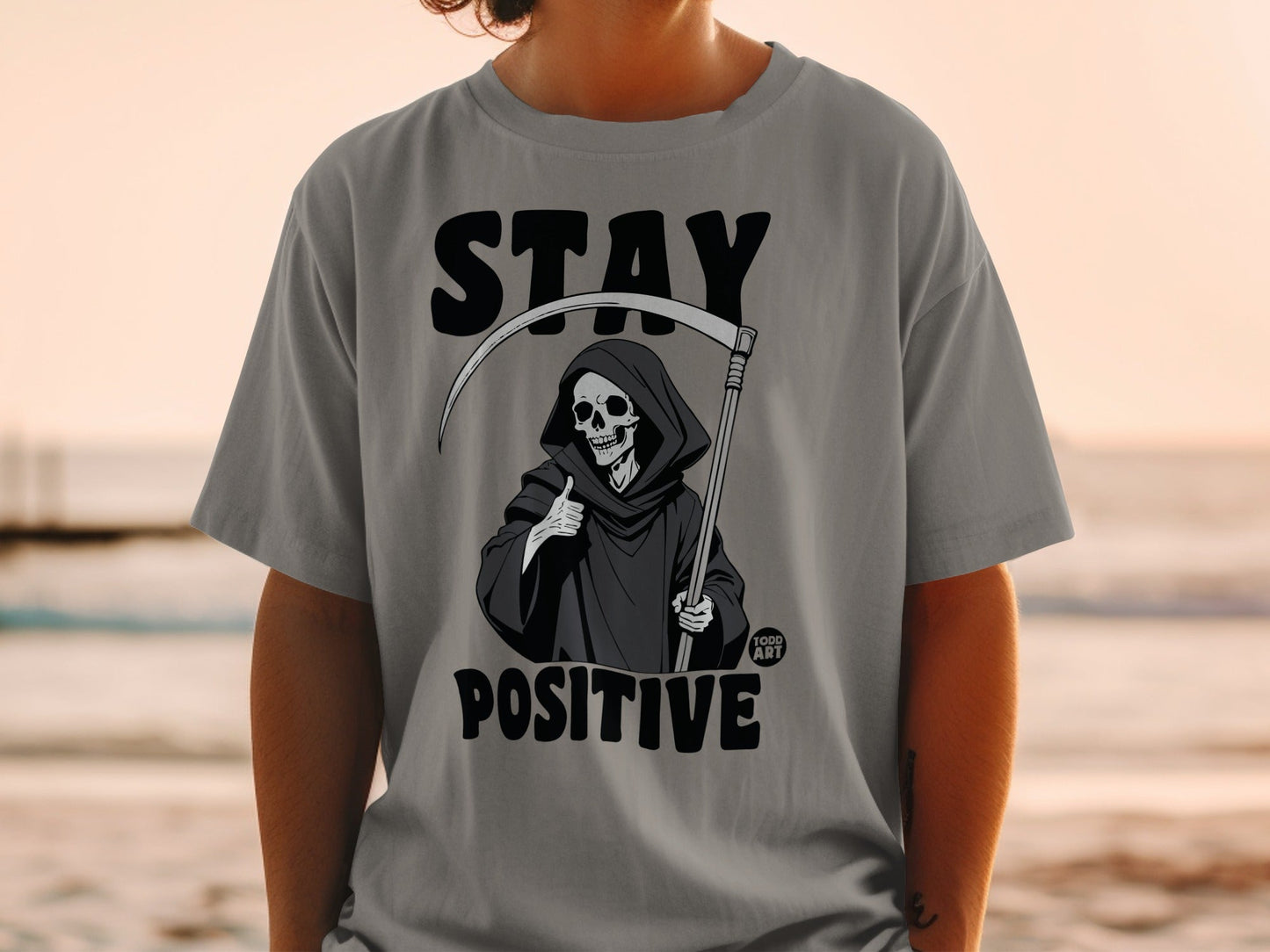Grim Reaper giving thumbs up on t-shirt, "STAY POSITIVE" text.