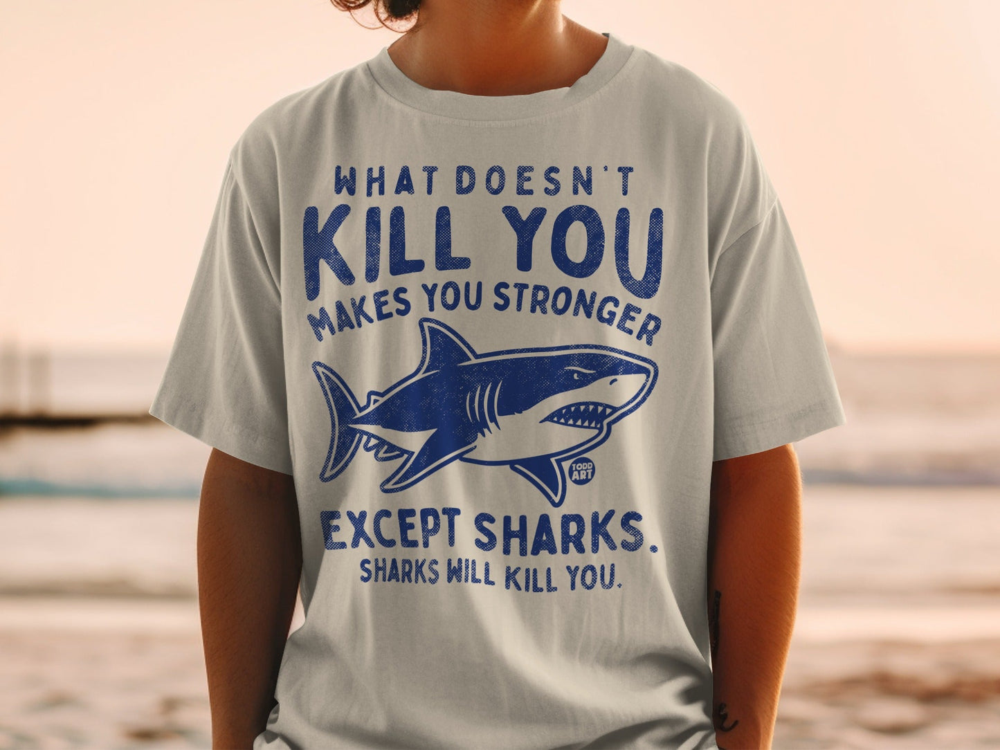 T-shirt with shark graphic and "What doesn't kill you makes you stronger except sharks" text.