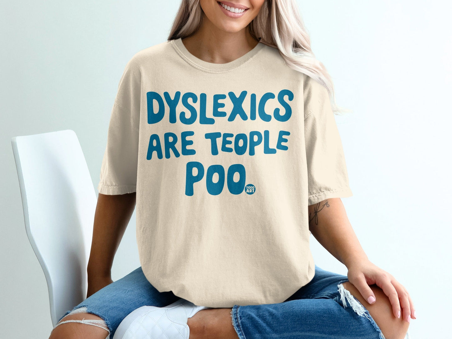 Unisex t-shirt with "Dyslexics Are Teople Poo" text in blue, worn by a woman.