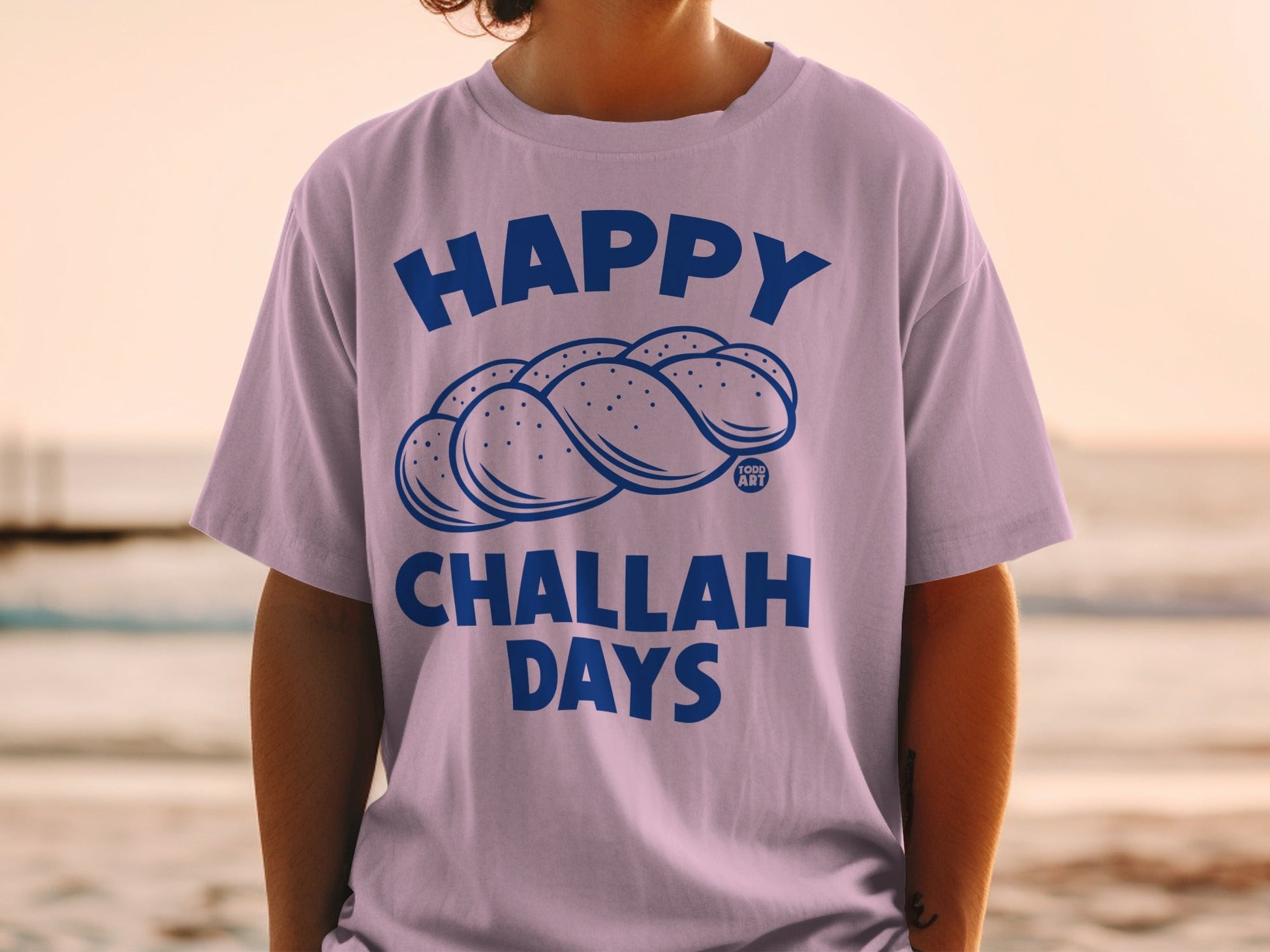 Purple t-shirt with "Happy Challah Days" and braided challah bread illustration.