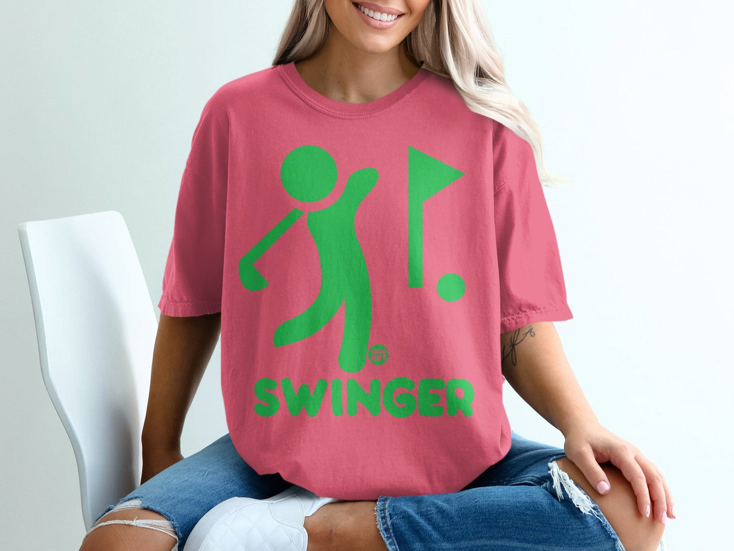 Coral t-shirt with green graphic of golfer and flag, text SWINGER.