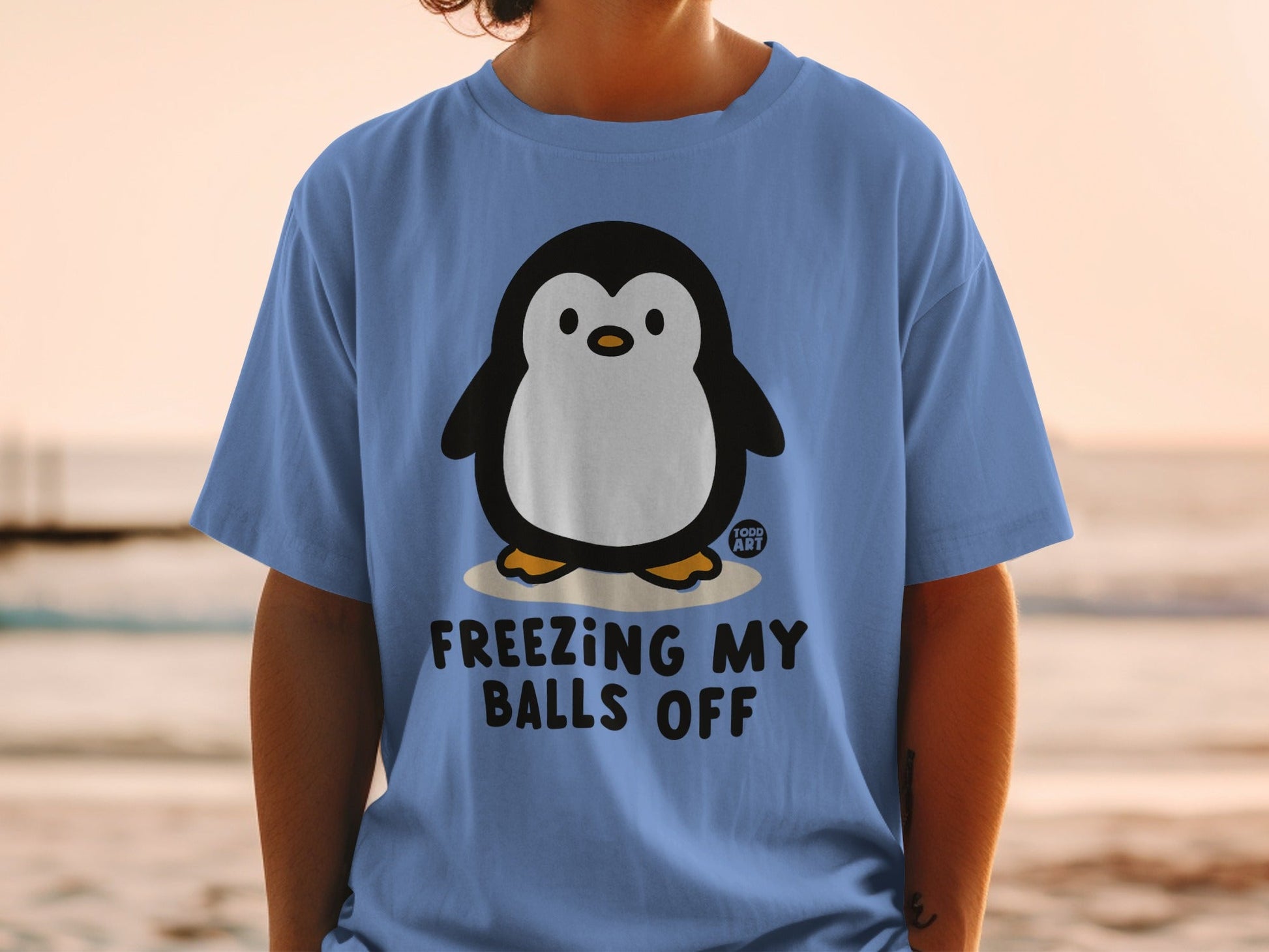 Blue t-shirt with cartoon penguin and text "FREEZING MY BALLS OFF".