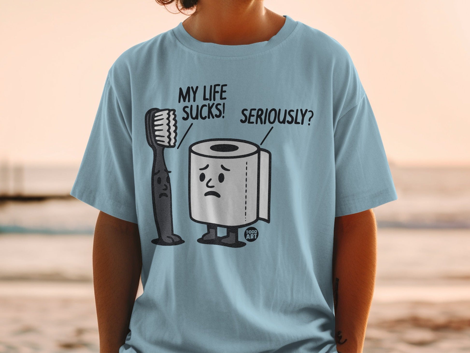 Light blue t-shirt with cartoon toothbrush and toilet paper expressing "My Life Sucks!"