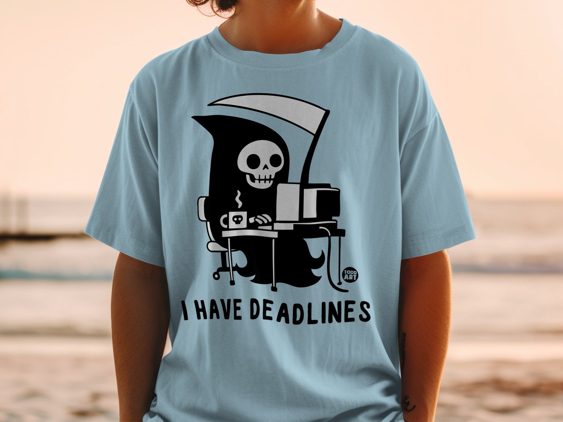 Grim reaper at a computer drinking coffee, with text "I HAVE DEADLINES" and "GOOD ART" logo.