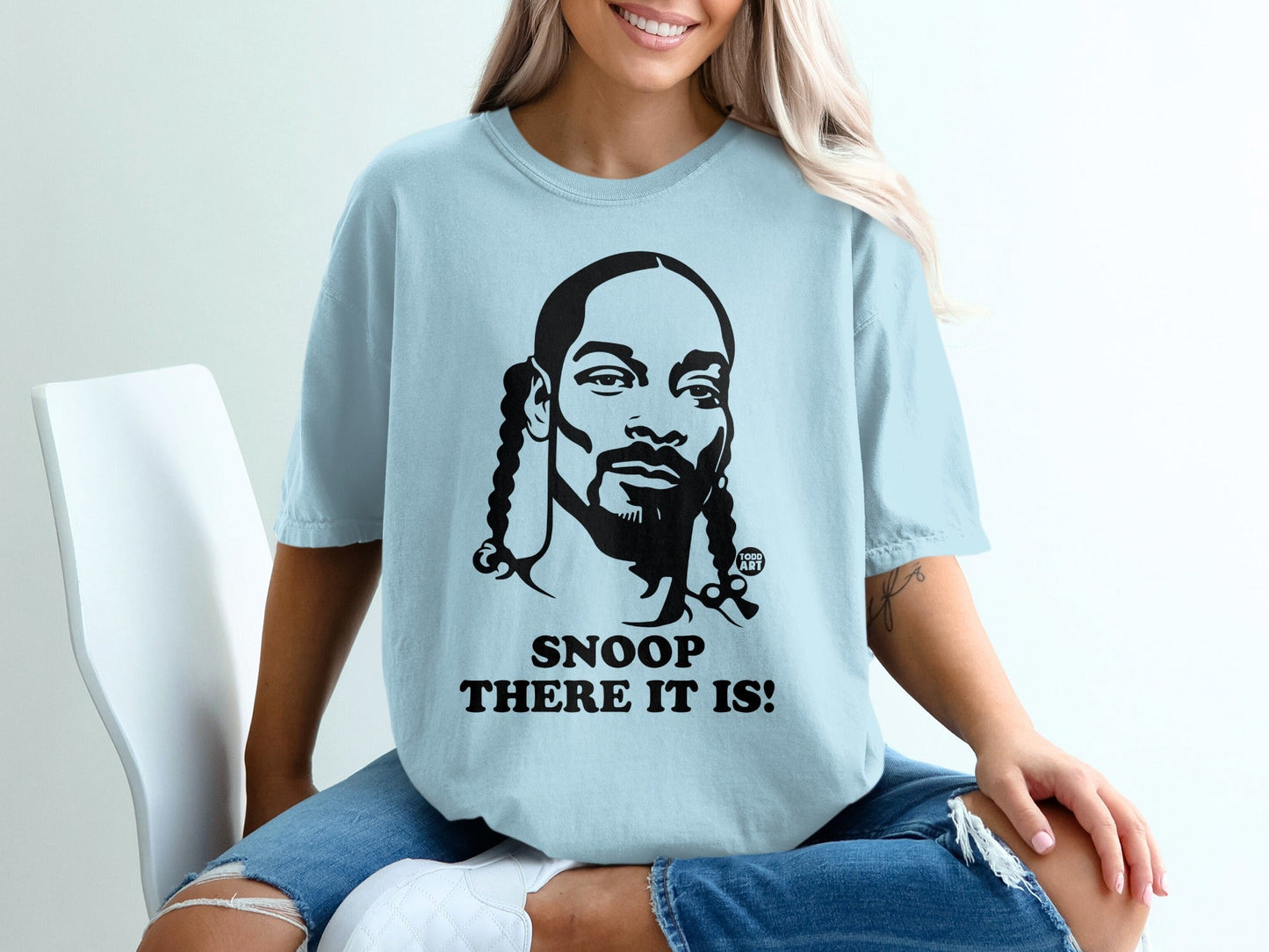 Light blue t-shirt with black graphic of Snoop Dogg and text "SNOOP THERE IT IS!".