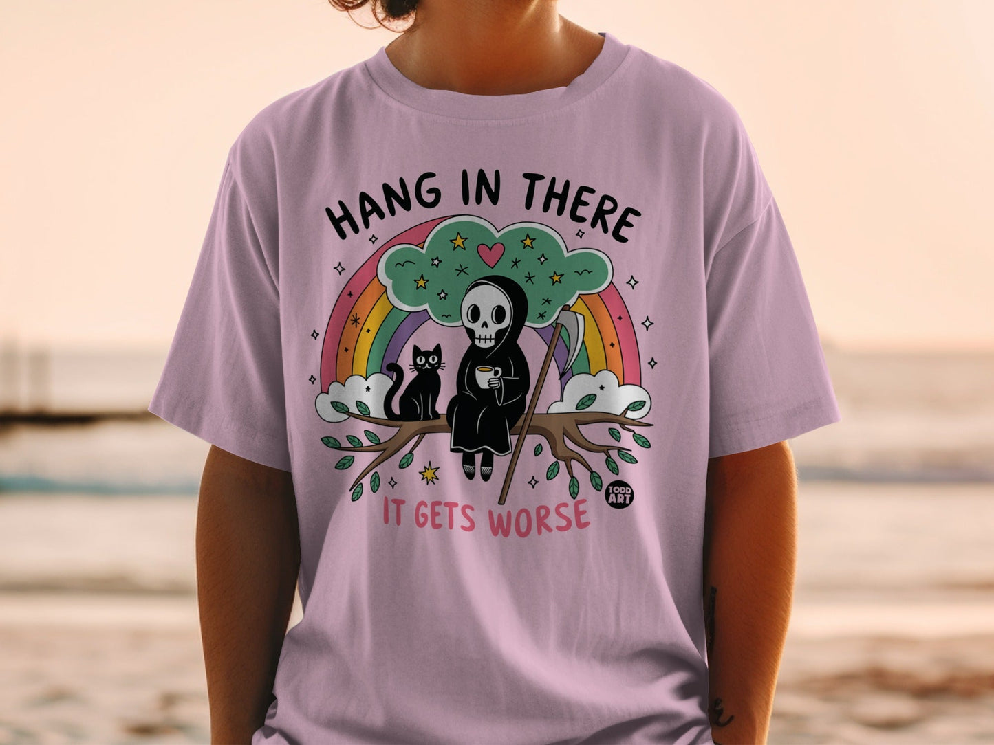 Lilac t-shirt with grim reaper and cat on a branch, text says "HANG IN THERE IT GETS WORSE."