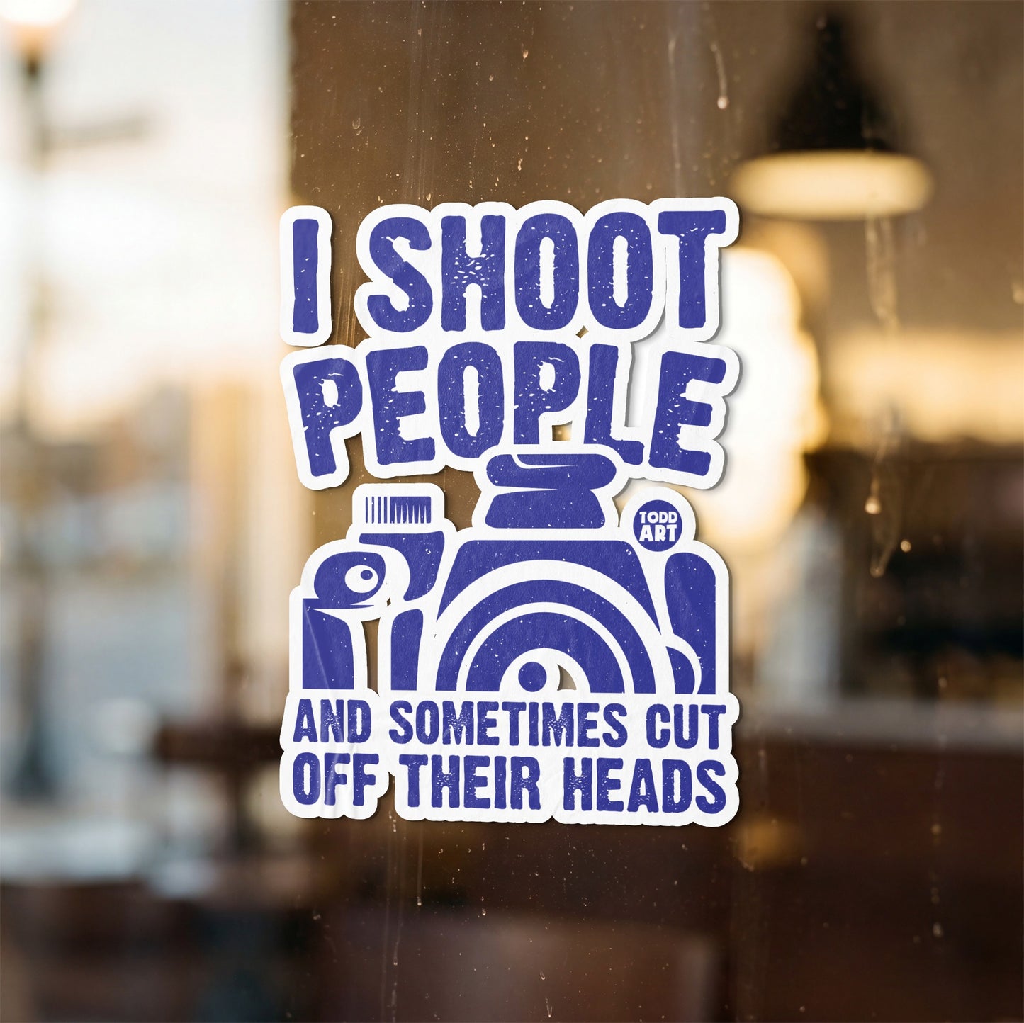 Blue sticker with text "I shoot people and sometimes cut off their heads" and a camera illustration.