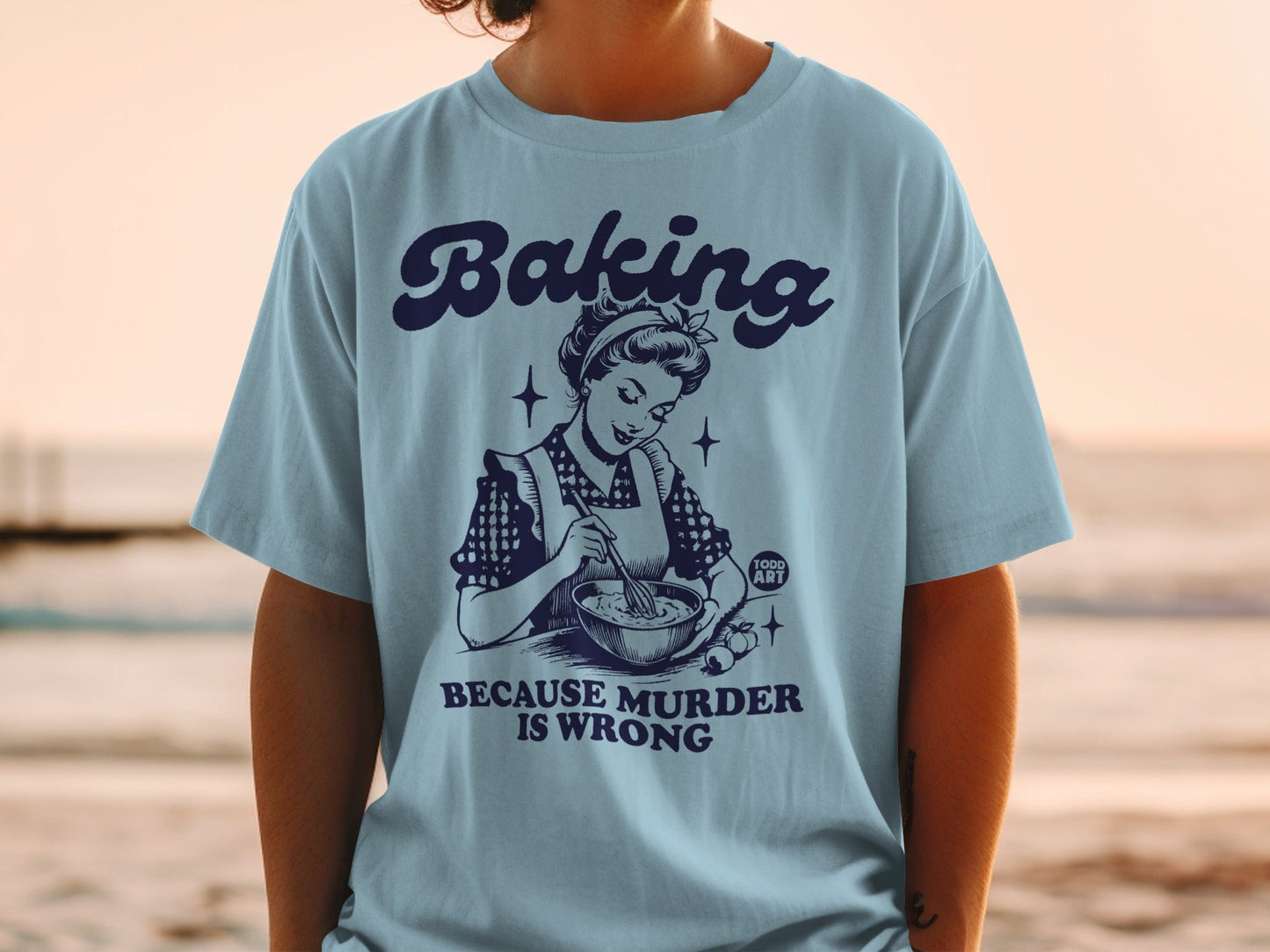 Blue t-shirt with retro graphic of woman baking, text reads "Baking is Wrong".