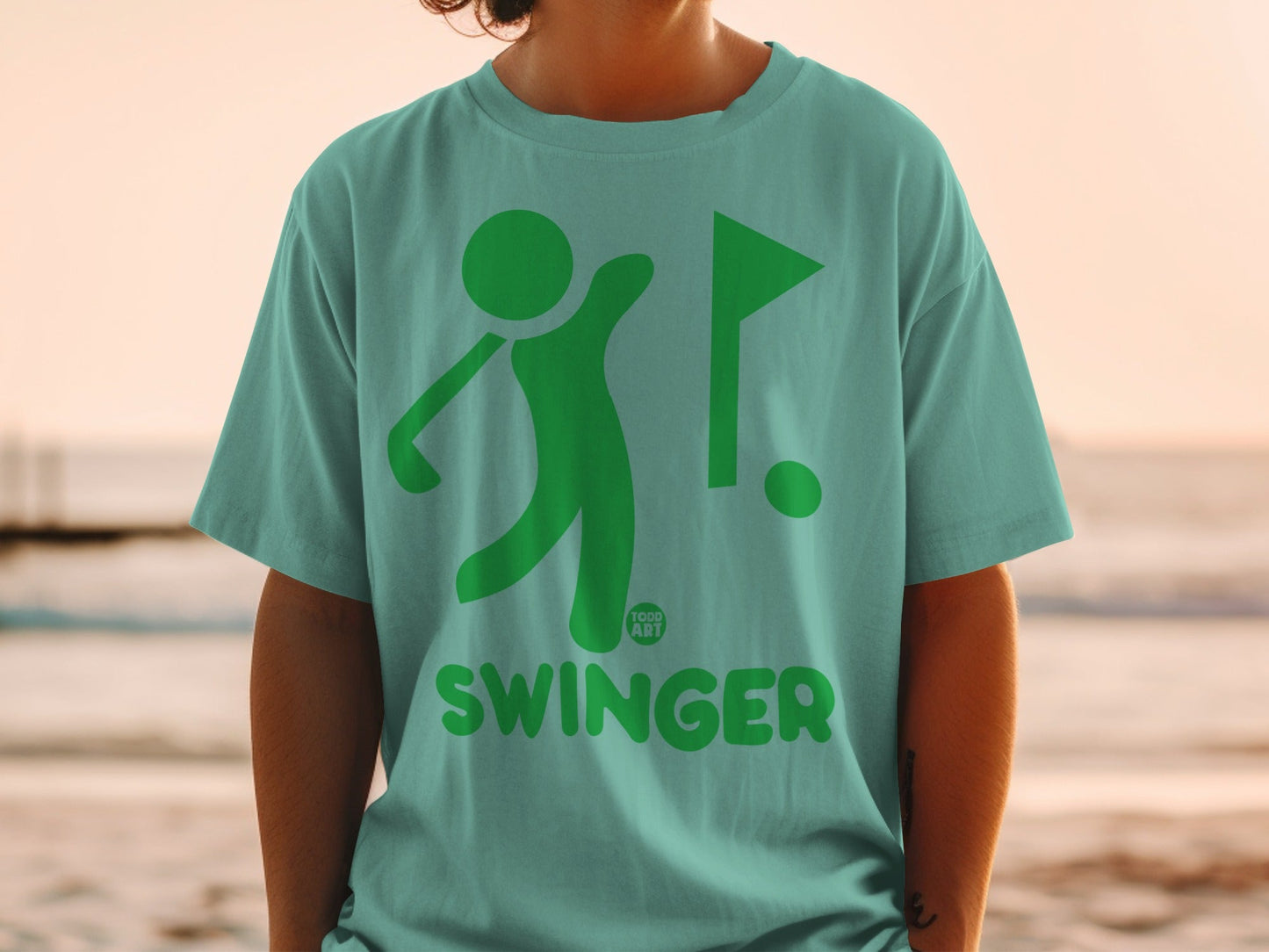 Green golf swing graphic and flag with "SWINGER" text on teal t-shirt.