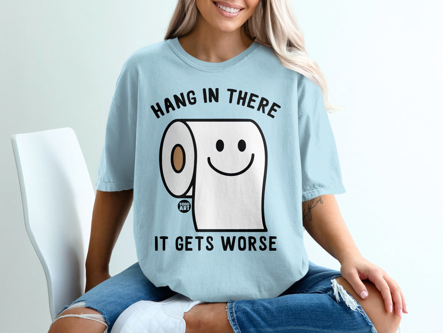 Light blue t-shirt with a cartoon toilet paper roll saying "Hang in there! It gets worse."