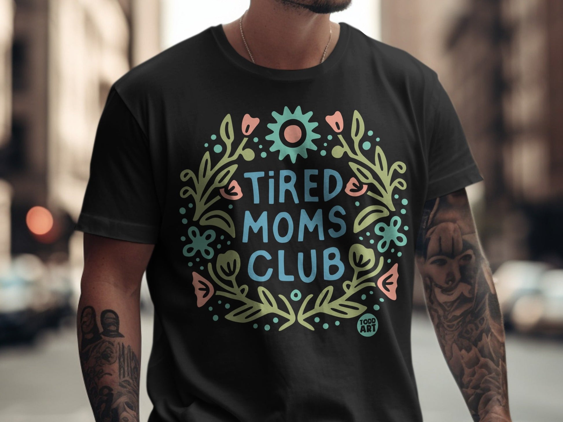 Black t-shirt with "Tired Moms Club" text in a floral wreath design.