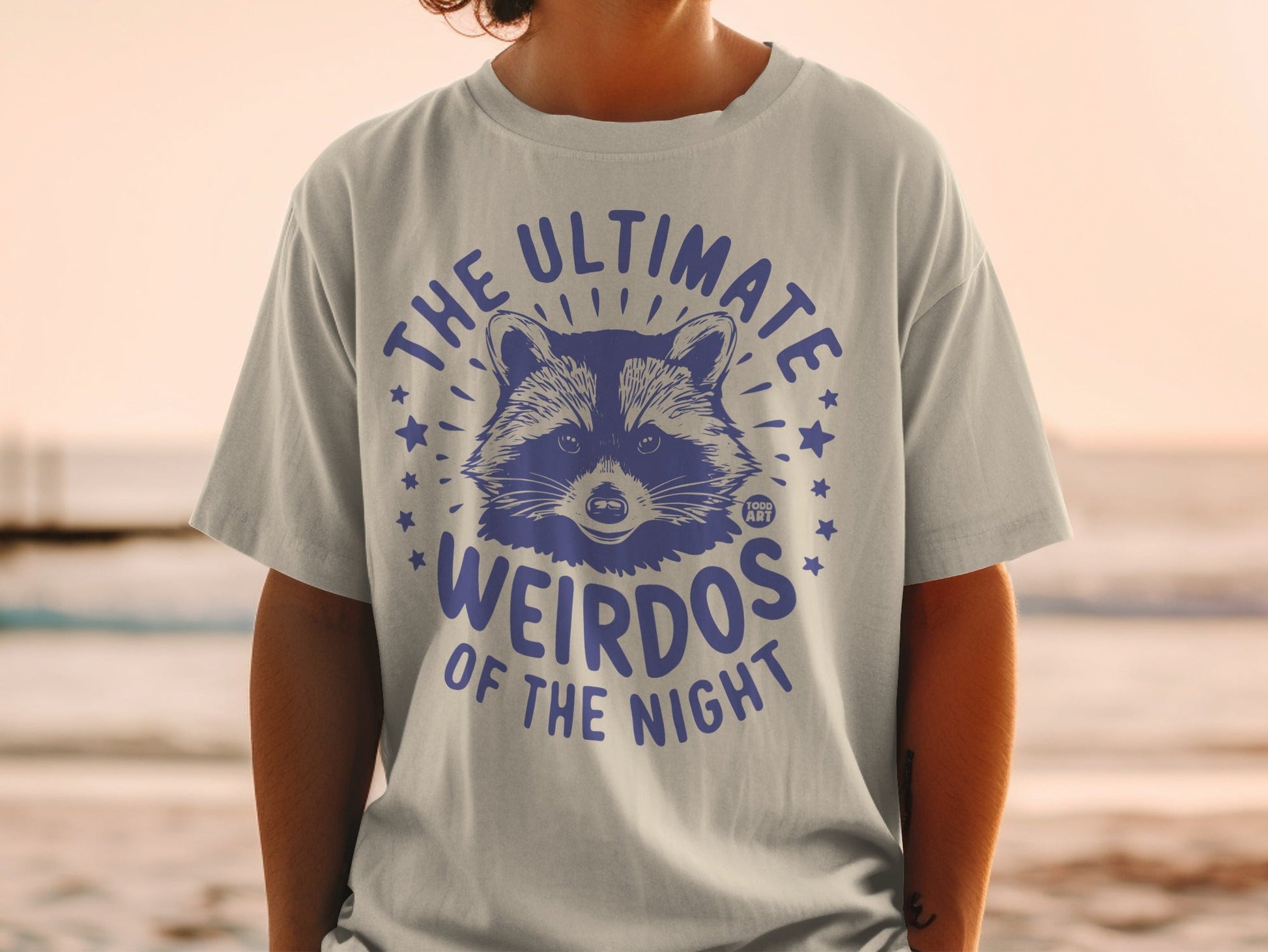 T-shirt with raccoon graphic and text "THE ULTIMATE WEIRDOS OF THE NIGHT".