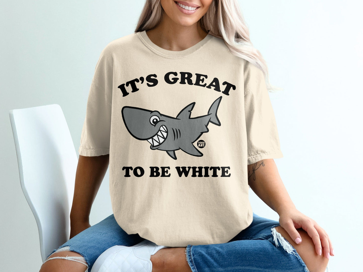 Light beige t-shirt with smiling shark graphic and text "IT'S GREAT TO BE WHITE".