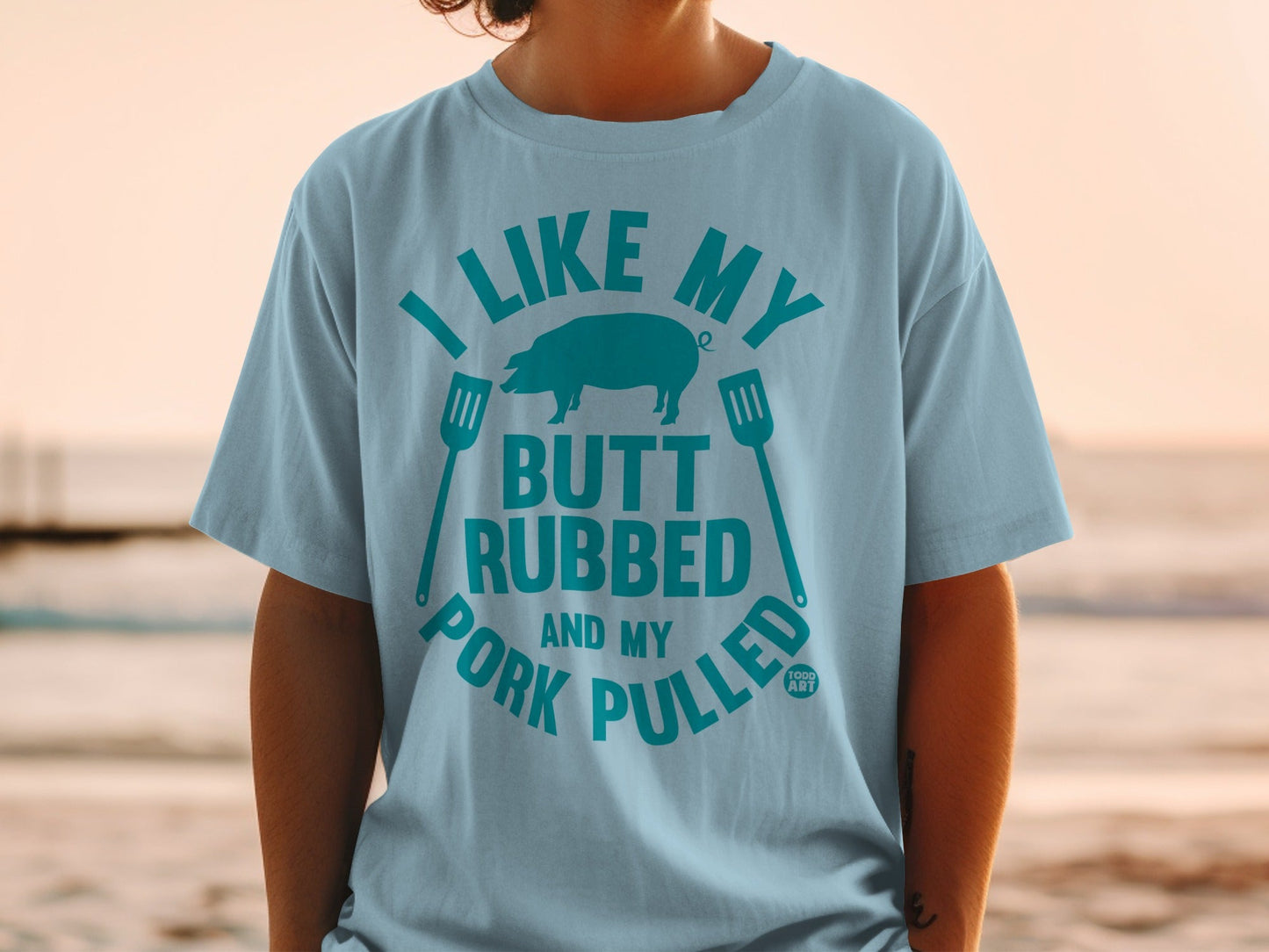 Light blue t-shirt with "I LIKE MY BUTT RUBBED AND MY PORK PULLED" text and pig graphic.