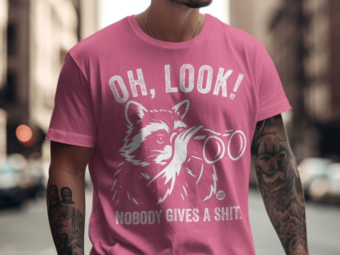 Pink t-shirt with raccoon looking through binoculars and text "OH, LOOK! NOBODY GIVES A SHIT."