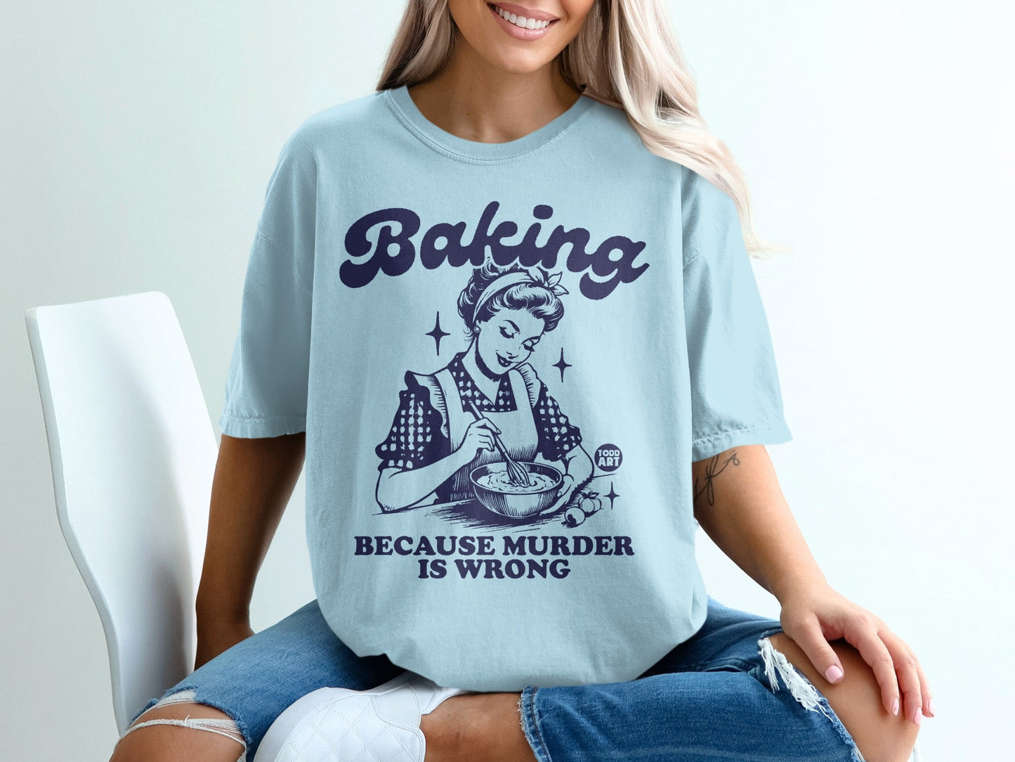 Light blue t-shirt with "Baking Because Murder Is Wrong" text and vintage woman baking graphic.