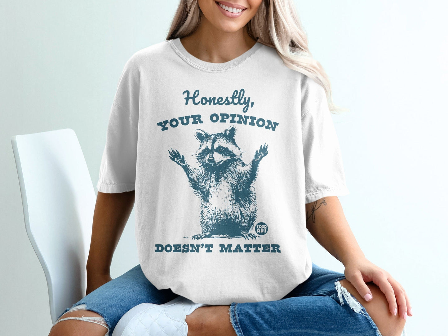 White t-shirt with a raccoon graphic and text "Honestly, YOUR OPINION DOESN'T MATTER".