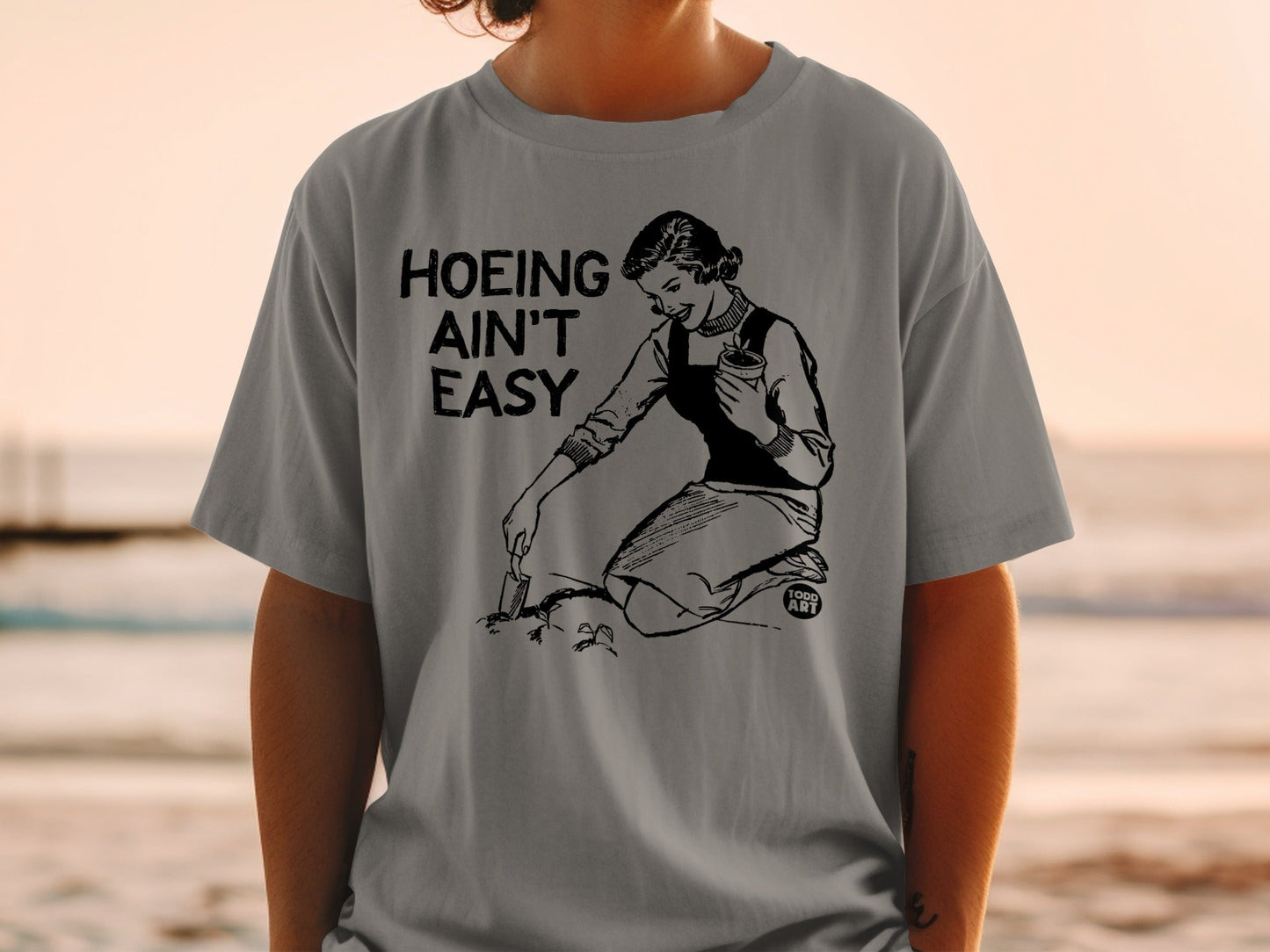 T-shirt graphic with text "Hoing Ain't Easy" and a woman gardening.
