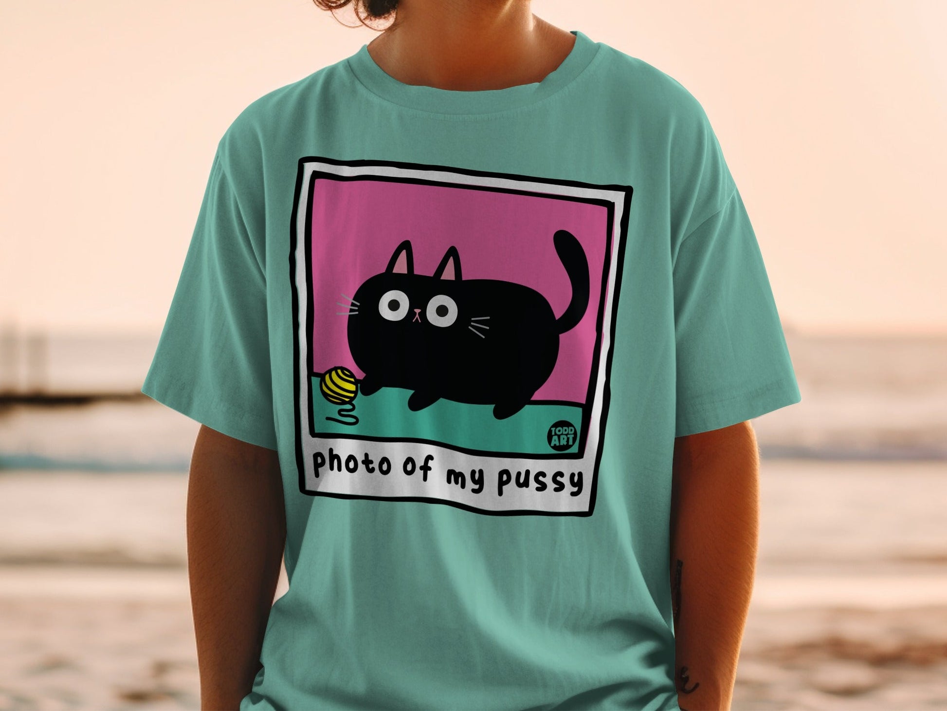 Teal t-shirt featuring a cartoon black cat playing with a yellow yarn ball.