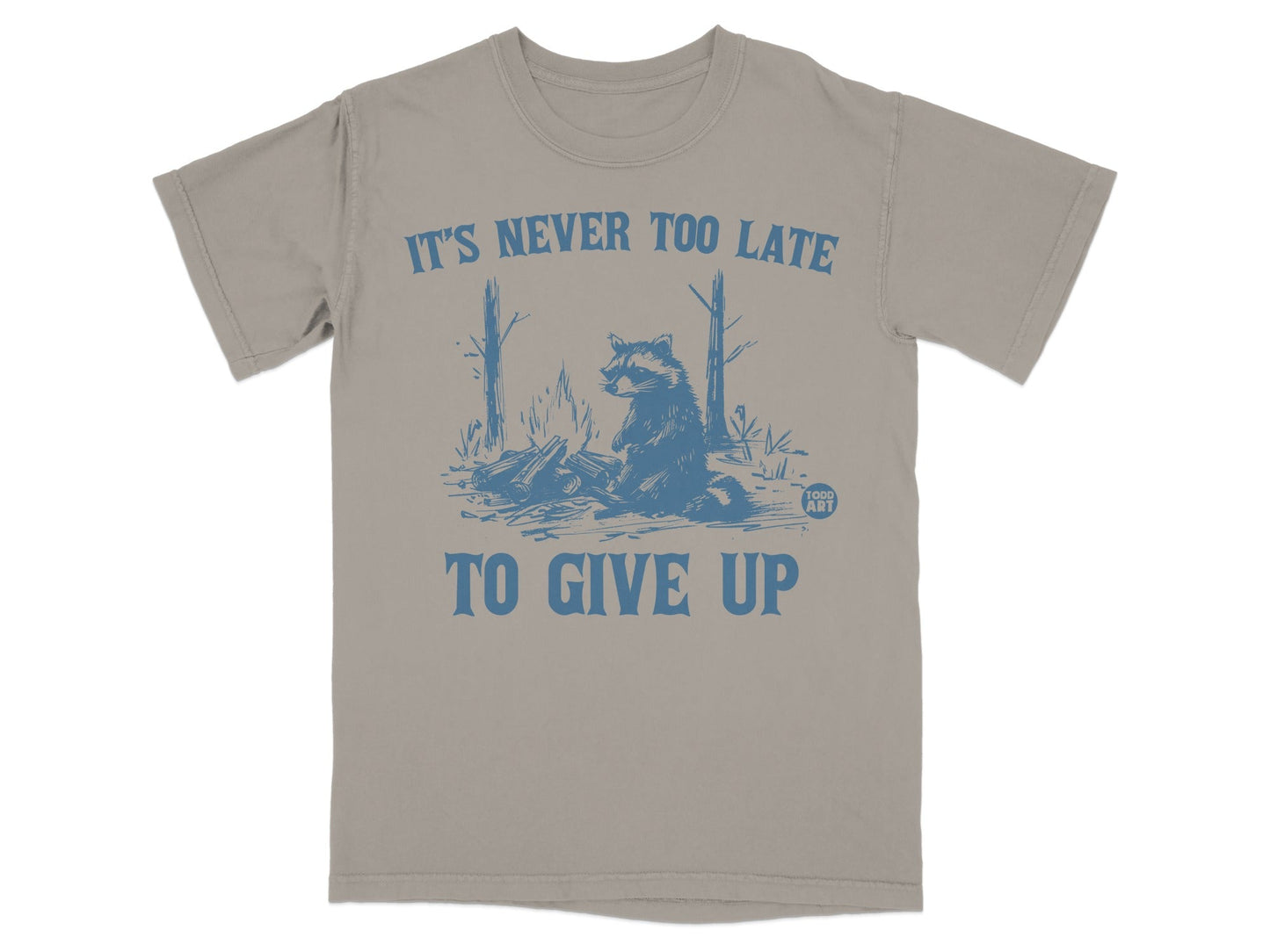 T-shirt with raccoon by campfire, text "IT'S NEVER TOO LATE TO GIVE UP".