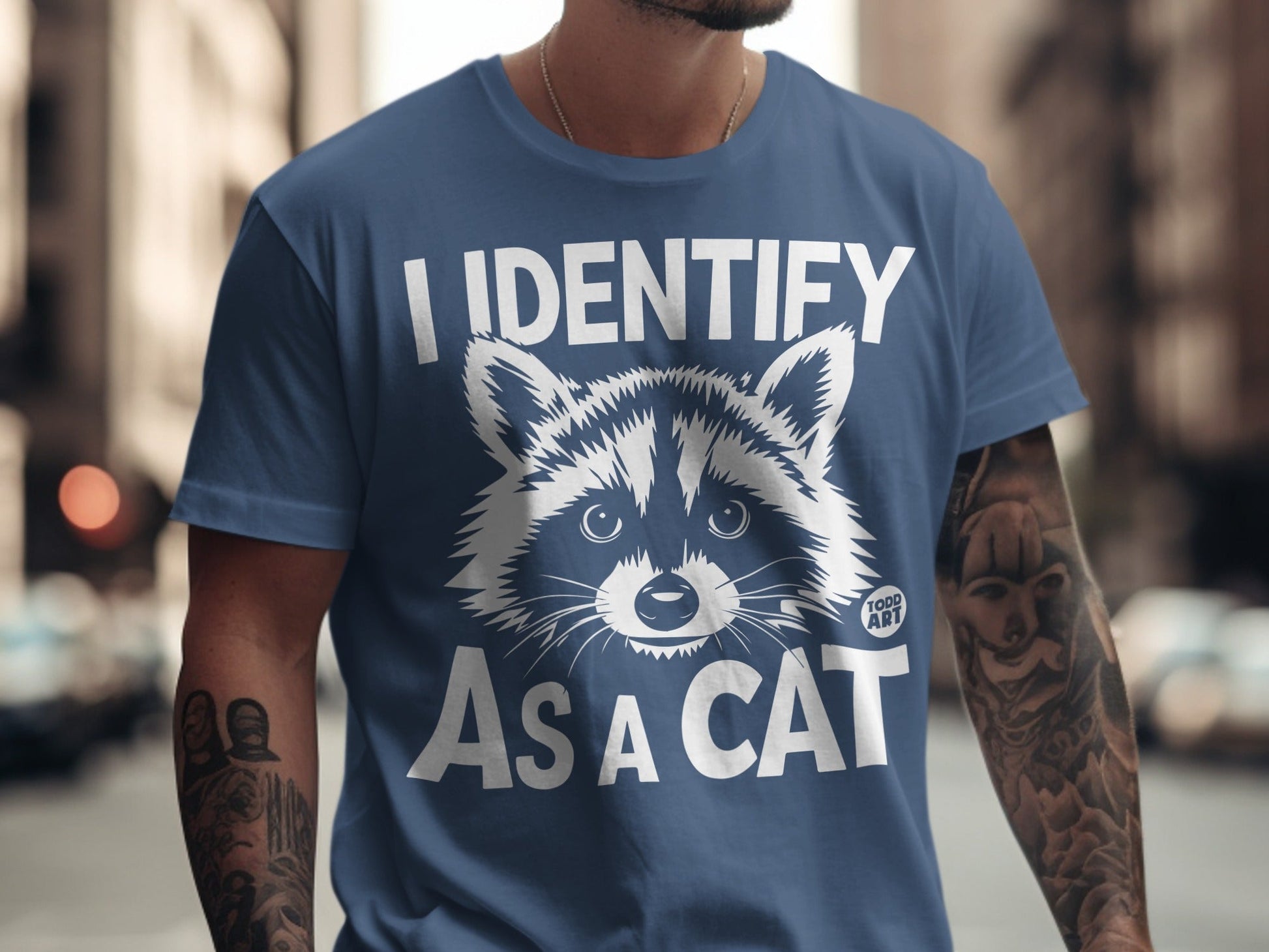 Blue t-shirt with a raccoon graphic and text "I IDENTIFY AS A CAT".