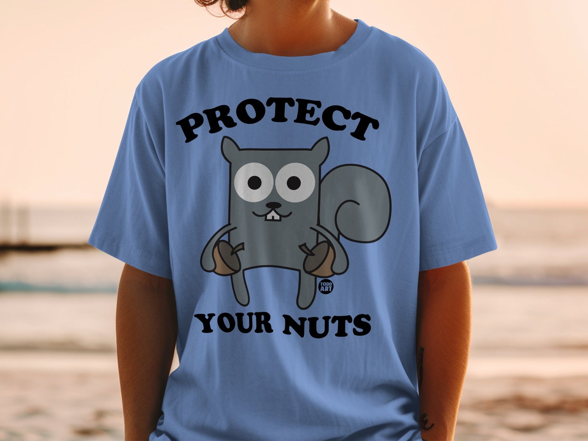 Blue t-shirt with cartoon squirrel holding acorns and text "PROTECT YOUR NUTS".