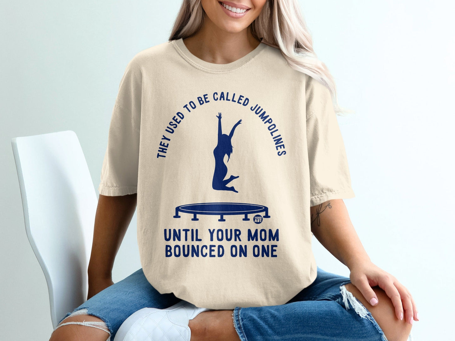 Cream t-shirt with blue text and trampoline graphic: "They used to be called jumplines until your mom bounced on one."