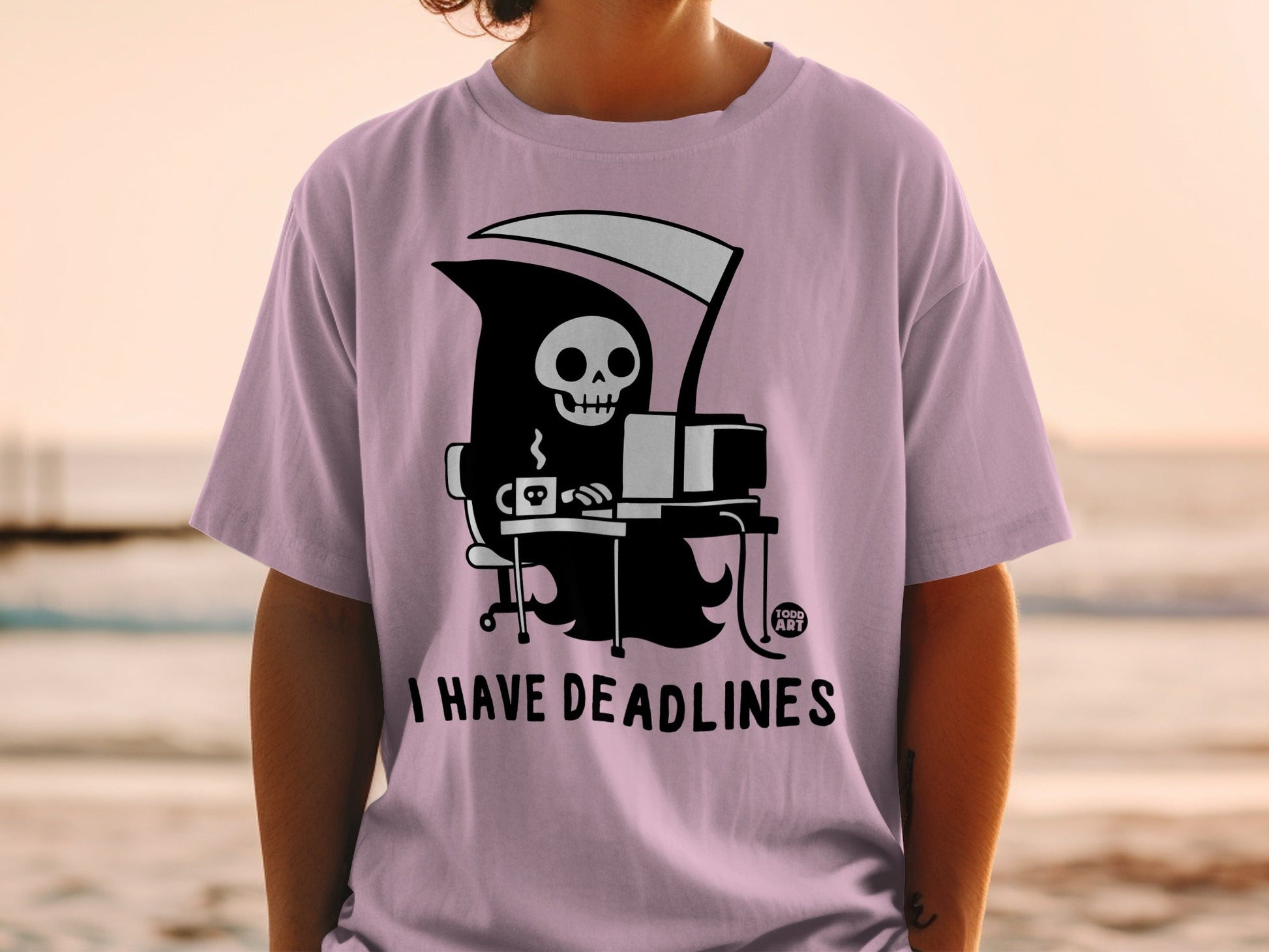 Grim reaper at a computer, "I HAVE DEADLINES" text on a pink t-shirt.