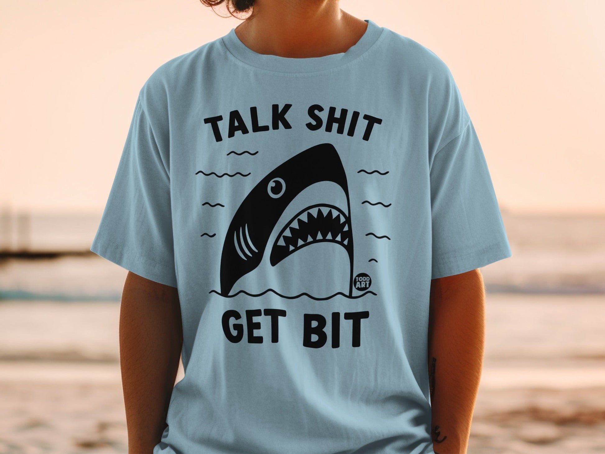Light blue t-shirt with black shark graphic and text "TALK SHIT GET BIT".