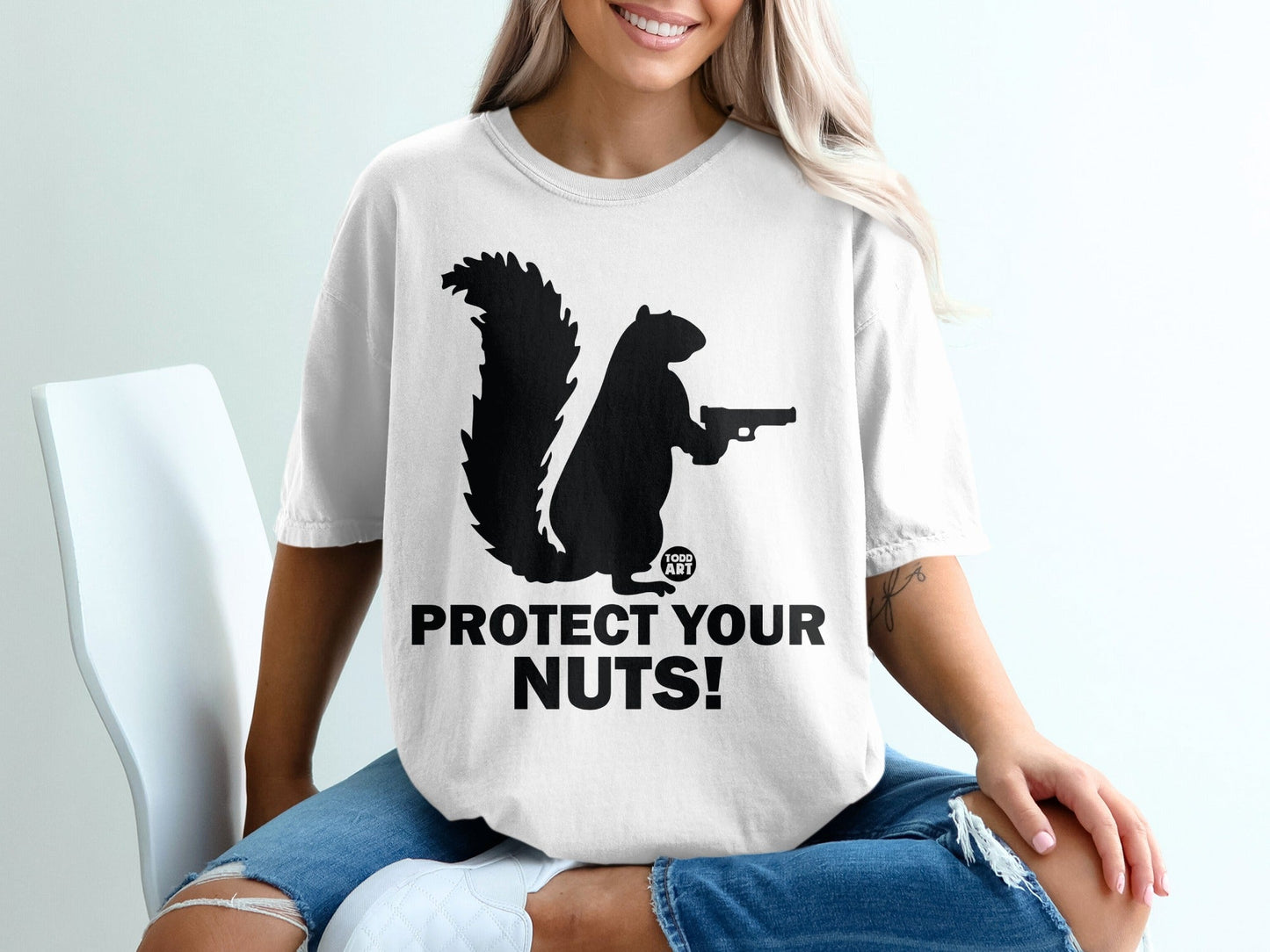 Black silhouette of a squirrel holding a gun on a white t-shirt, reading "PROTECT YOUR NUTS!".