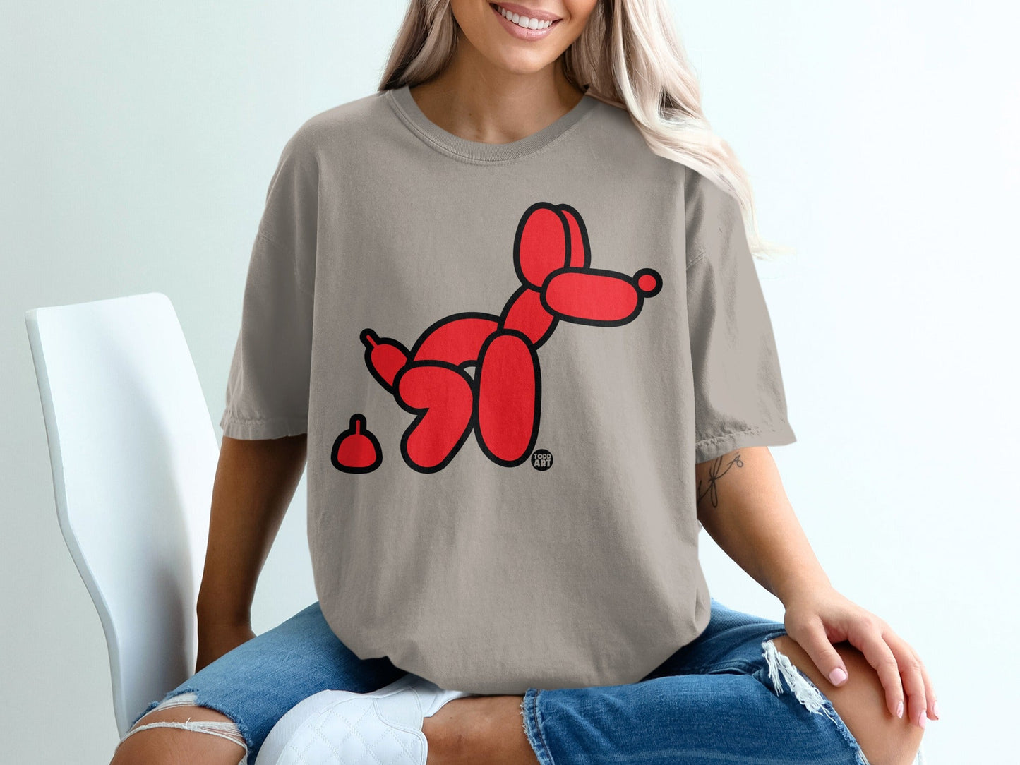 Red balloon dog with a small poop in front on a taupe t-shirt.
