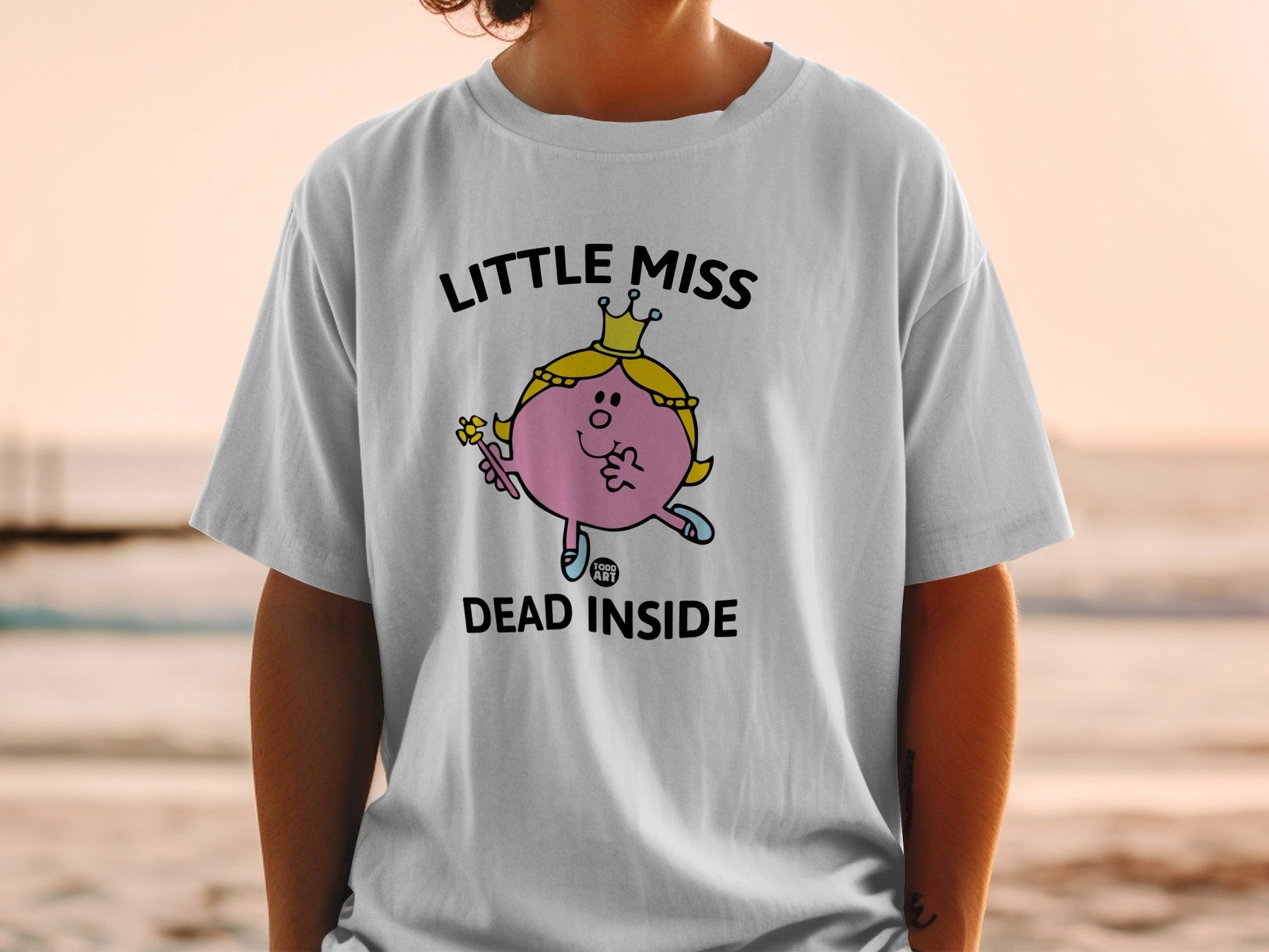 White t-shirt with "Little Miss Dead Inside" graphic of a character holding a wand.