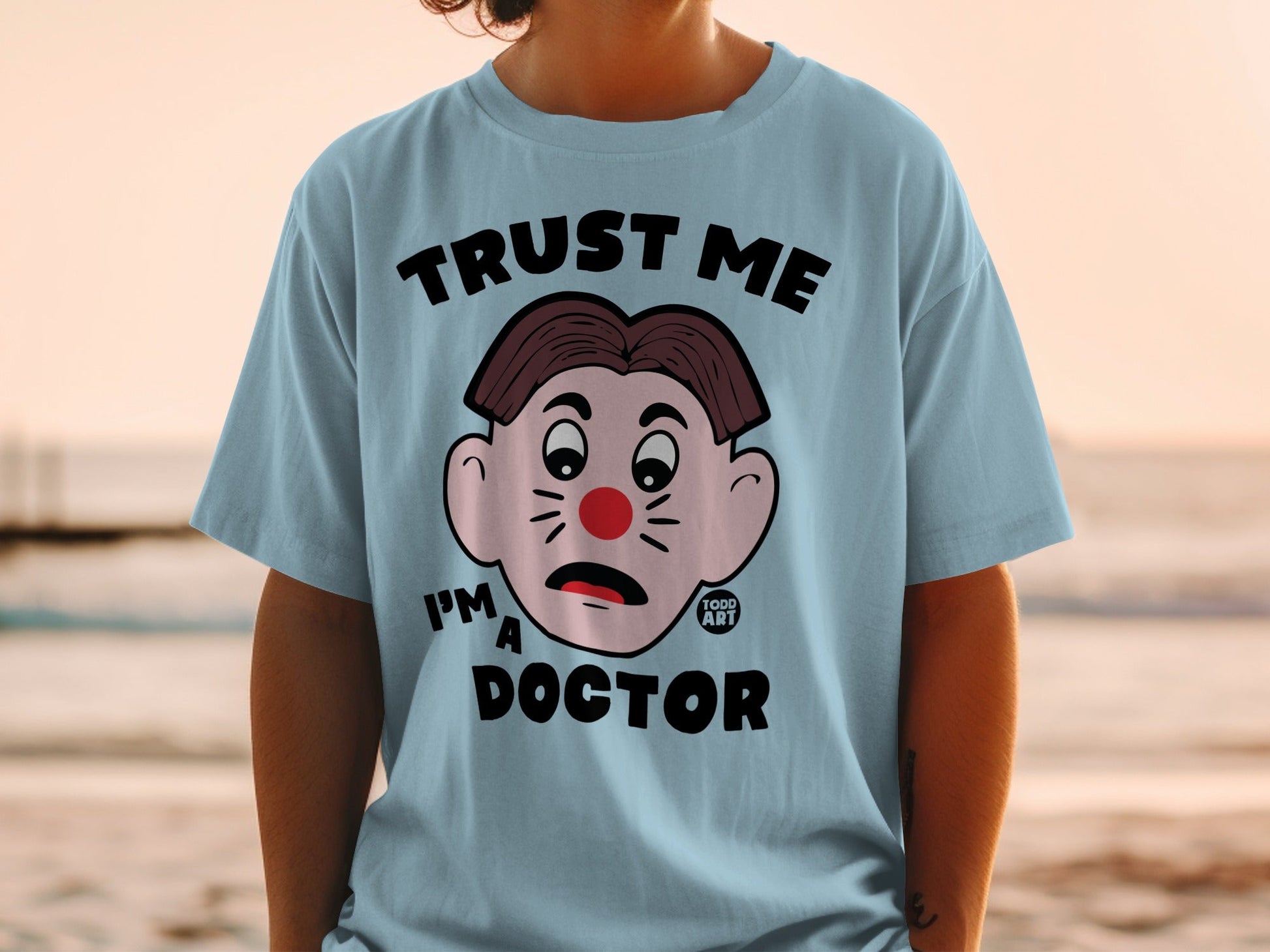 Light blue t-shirt with cartoon clown face and "TRUST ME I'M A DOCTOR" text.