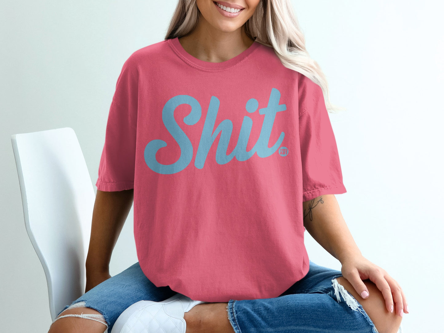 Coral t-shirt with "Shit" printed in light blue script.