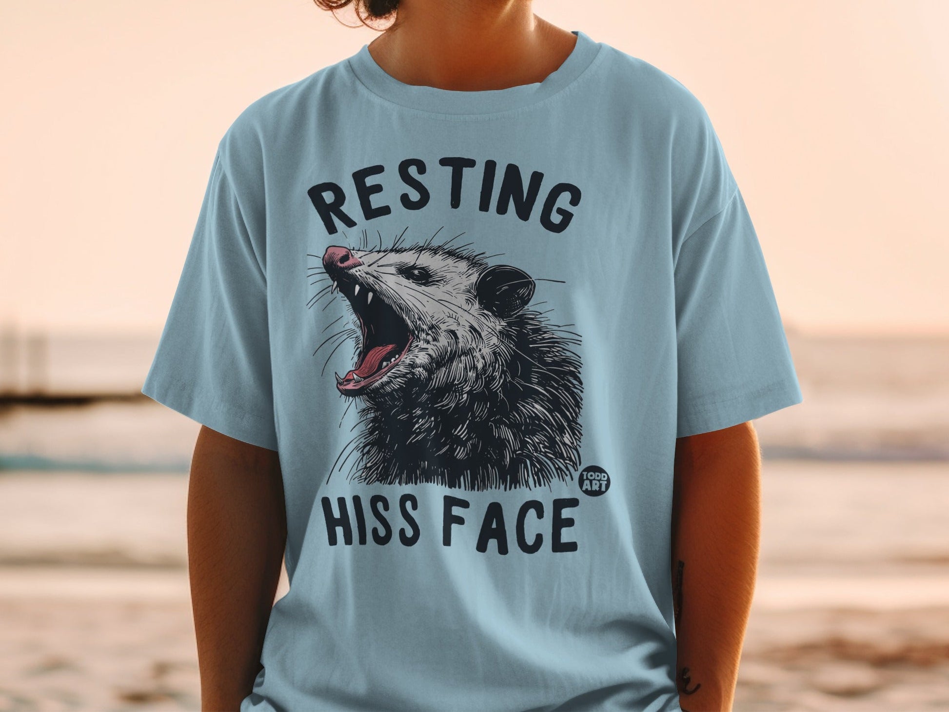 Light blue t-shirt with a graphic of a hissing possum and text.